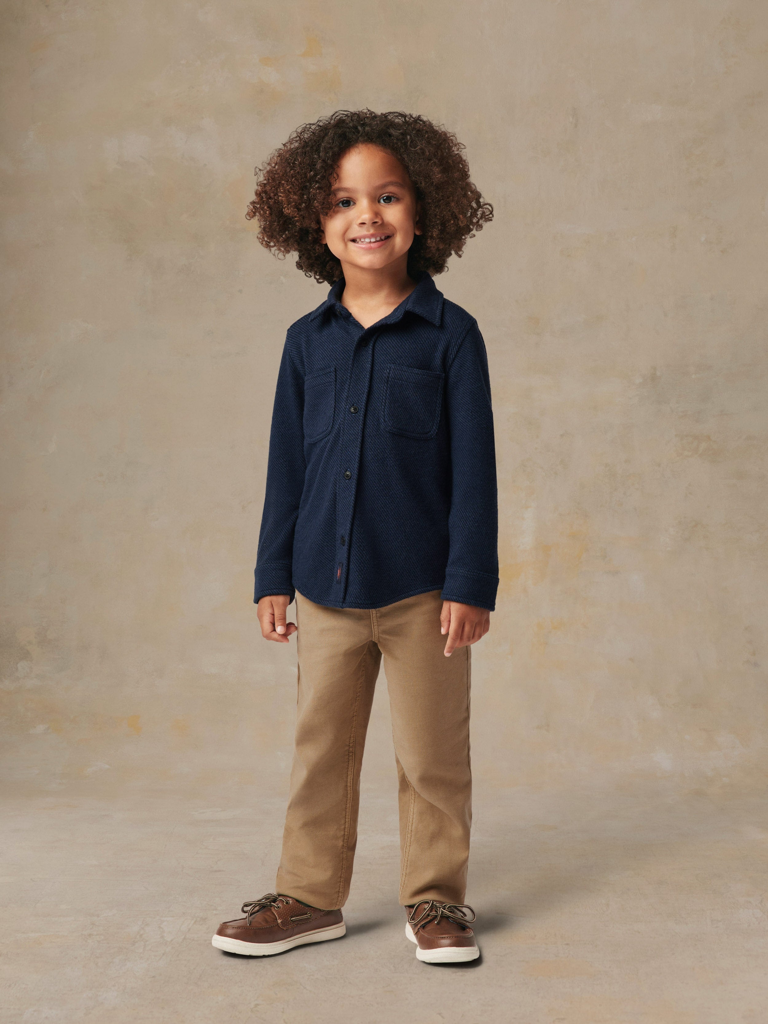 A child wearing a blue button up shirt and beige pants
