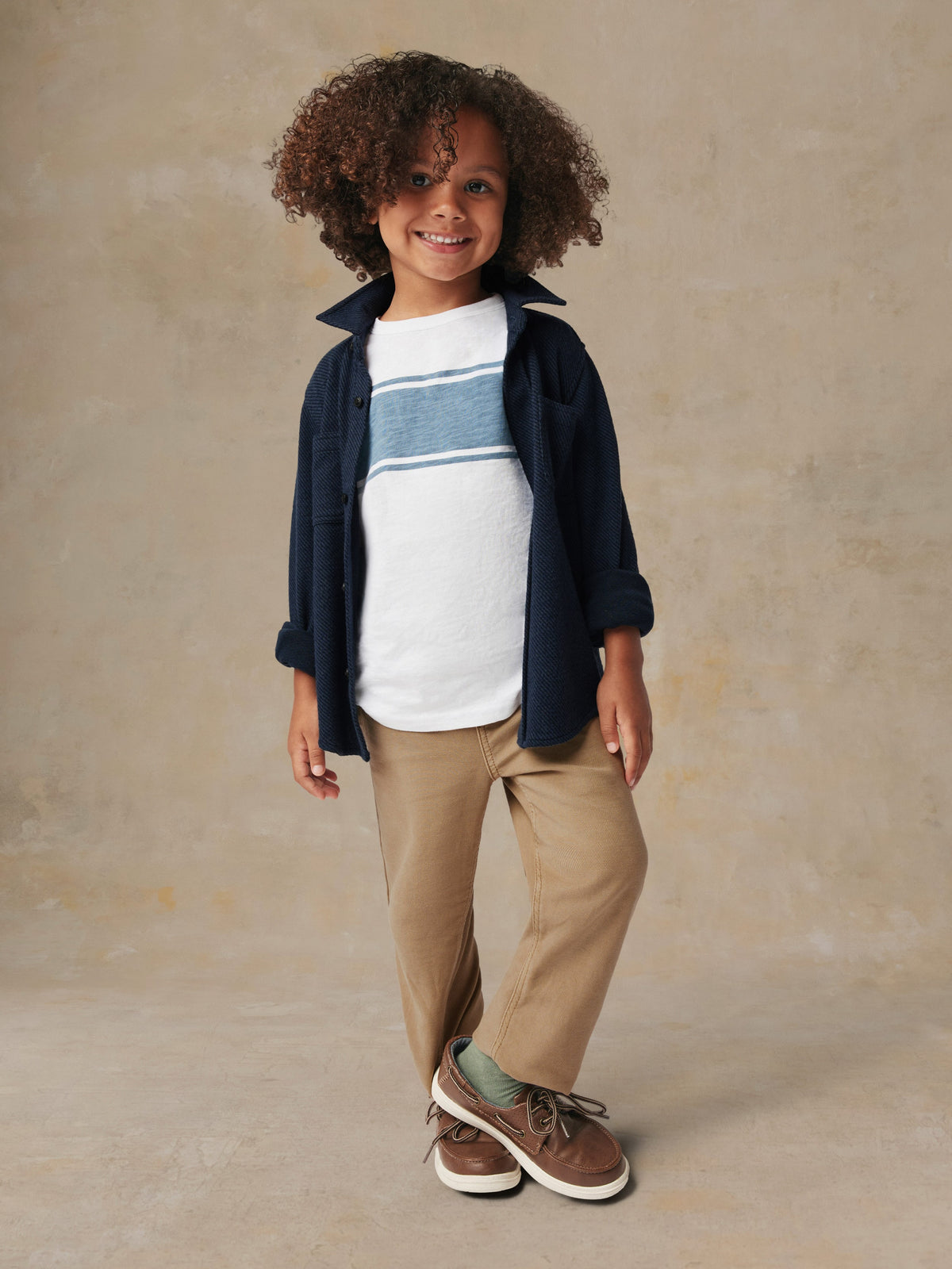A child wearing a blue button up shirt and beige pants, image 4 of 6