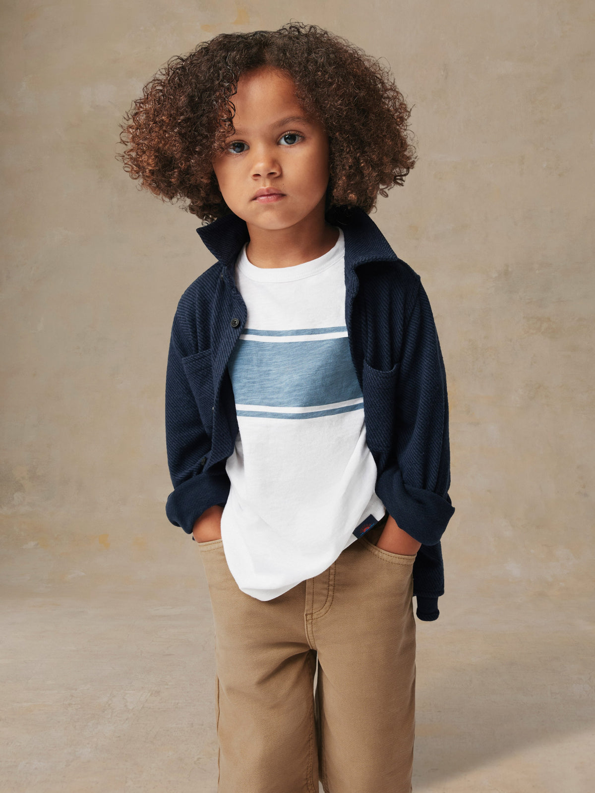 Close up of a child wearing a blue button up shirt and beige pants, image 2 of 6