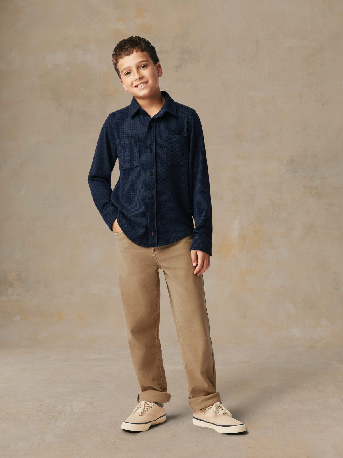 A child wearing a blue button up shirt and beige pants, image 1 of 6