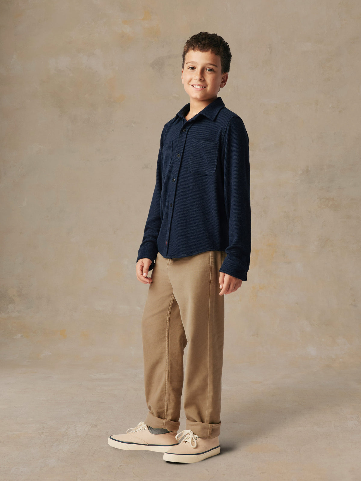 A child wearing a blue button up shirt and beige pants, image 3 of 6