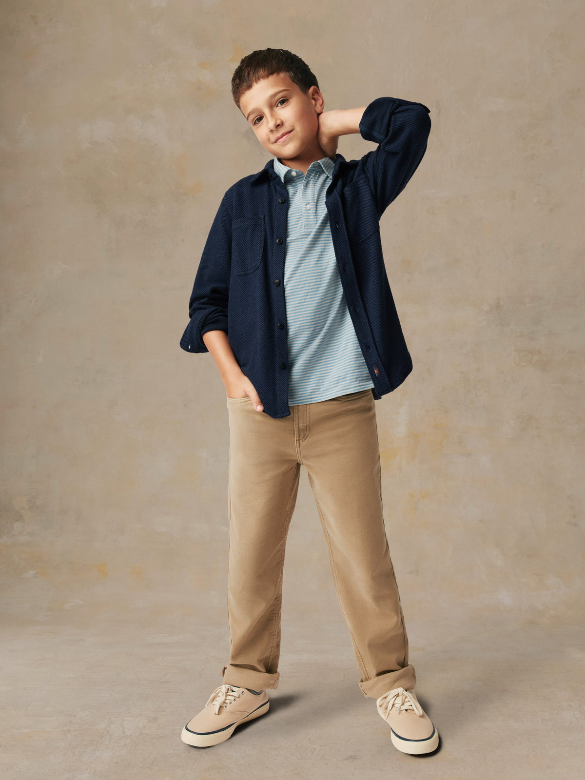 A child wearing a blue button up shirt and beige pants, image 4 of 6