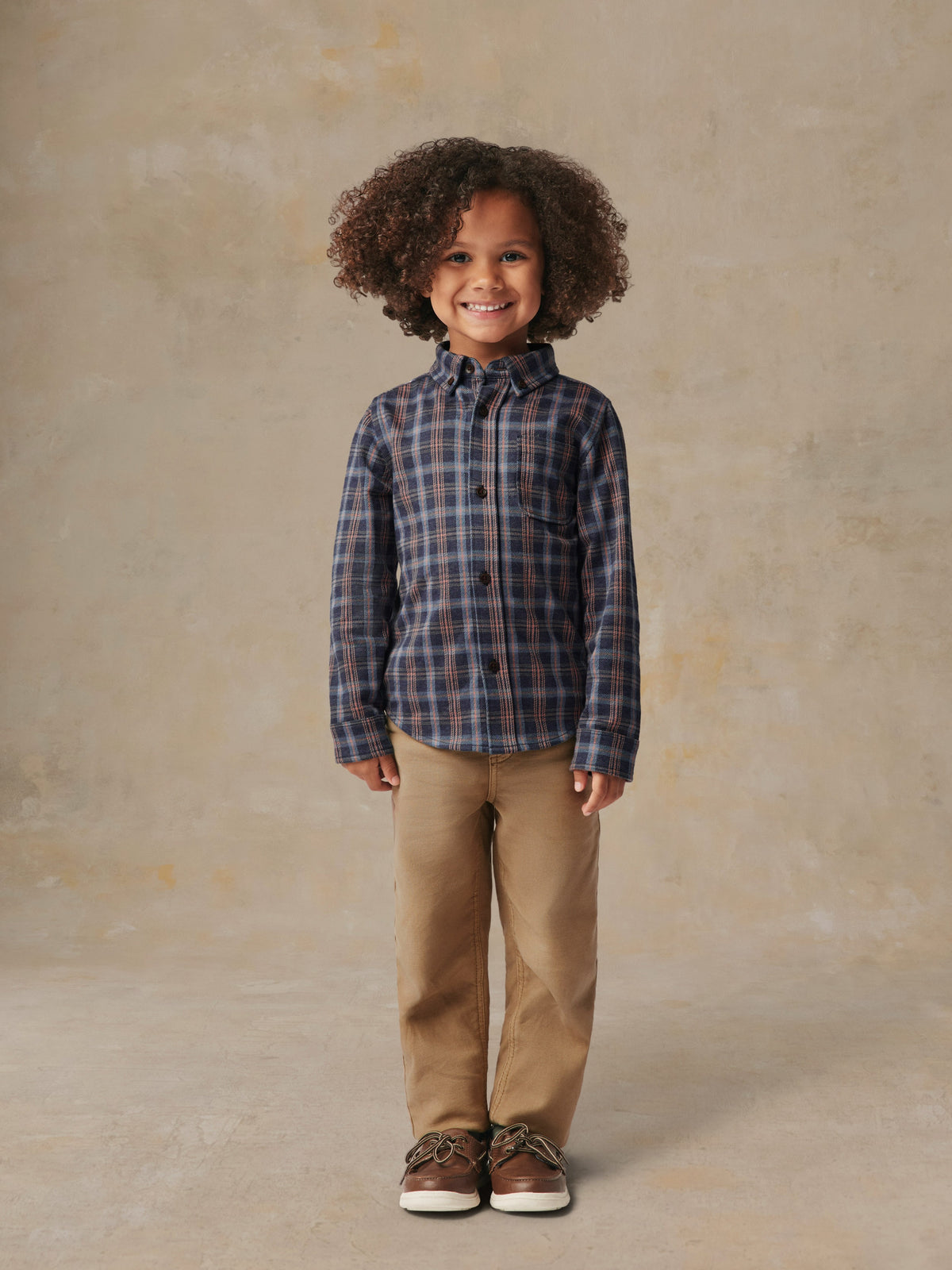 A child is wearing a plaid shirt and beige pants, image 5 of 6