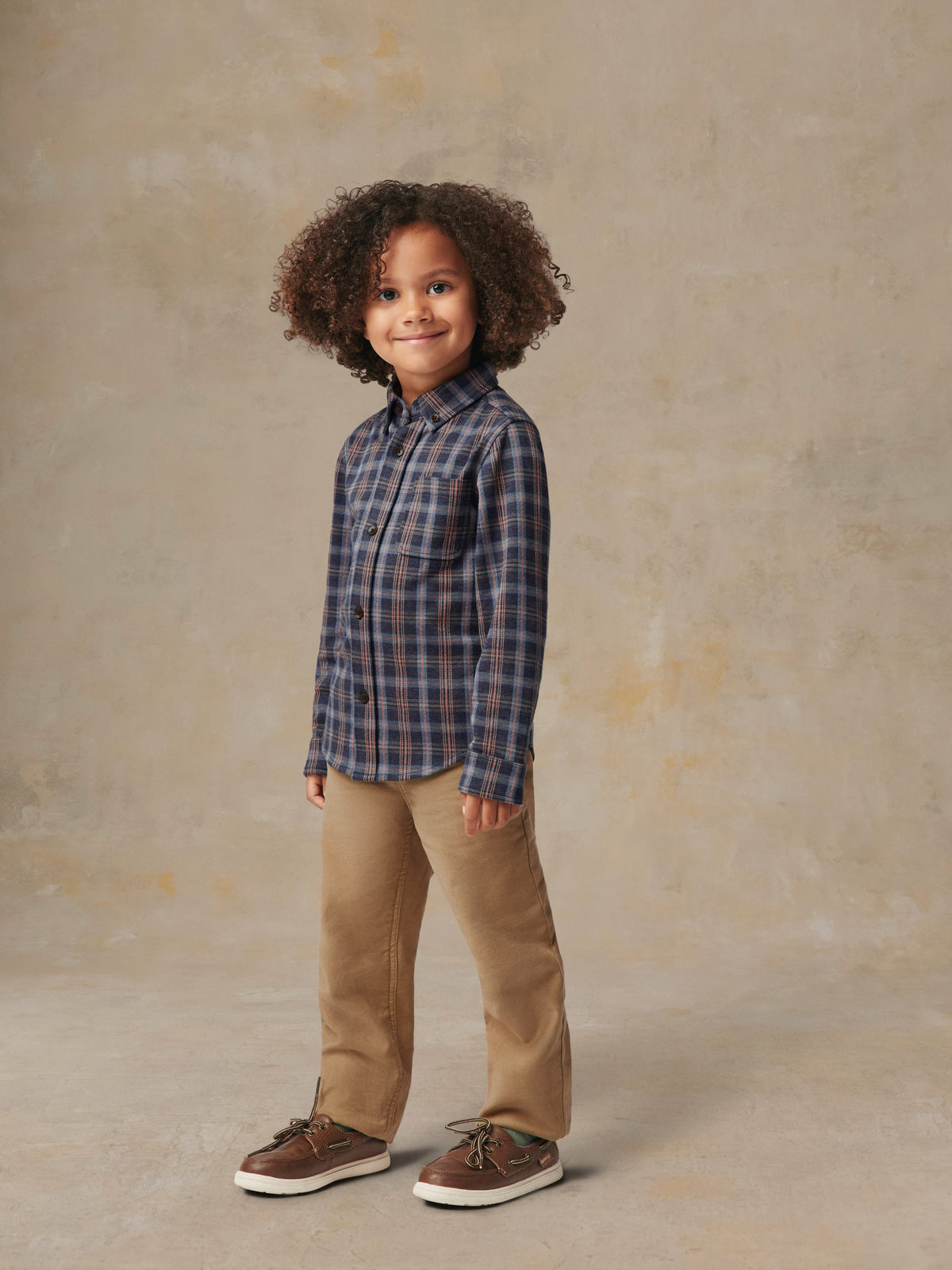 A child is wearing a plaid shirt and beige pants, image 1 of 6