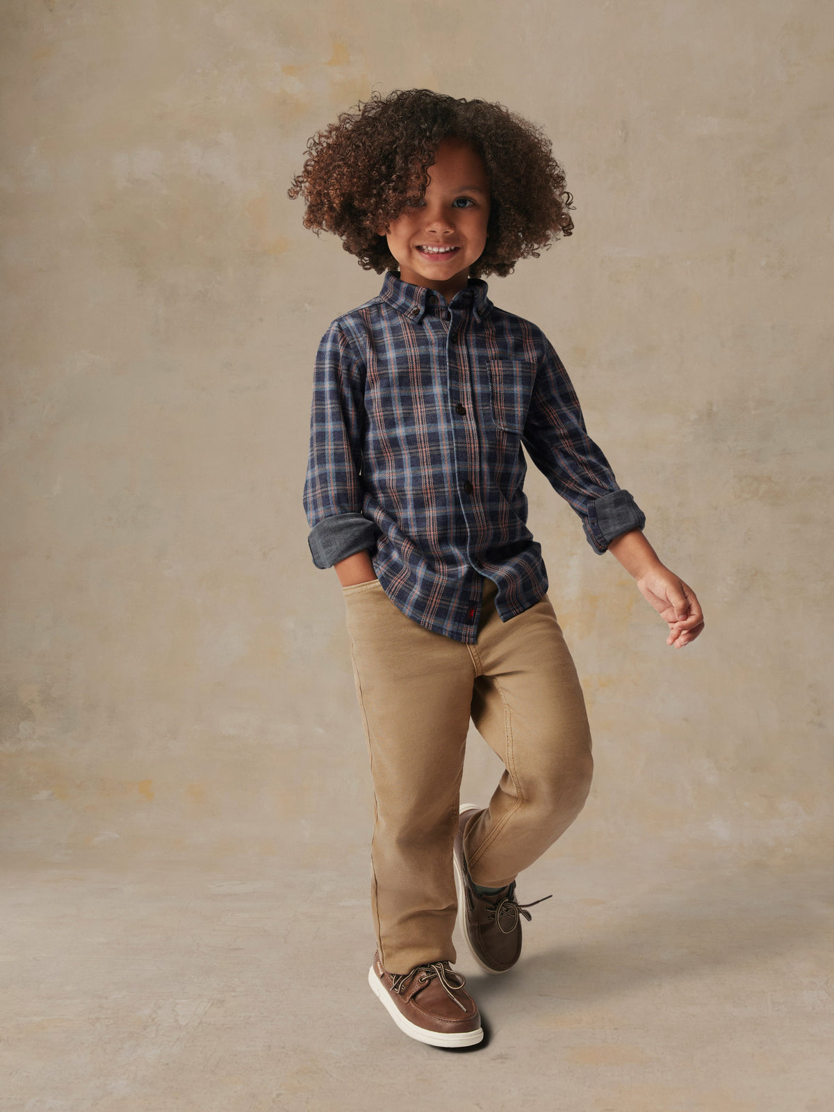 A child is wearing a plaid shirt and beige pants, image 3 of 6