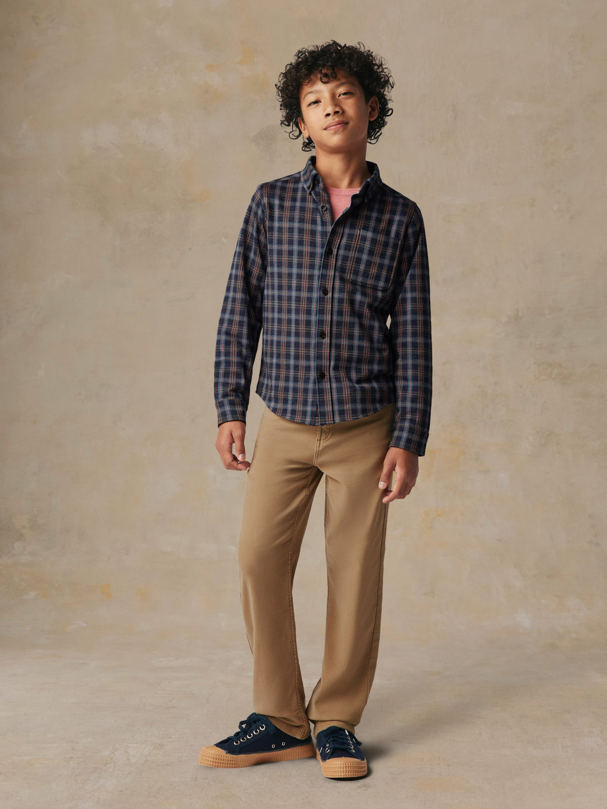A child wearing a plaid button down shirt and beige pants, image 2 of 7