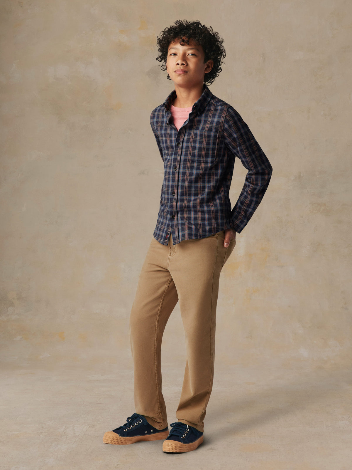 A child wearing a plaid button down shirt and beige pants, image 6 of 7