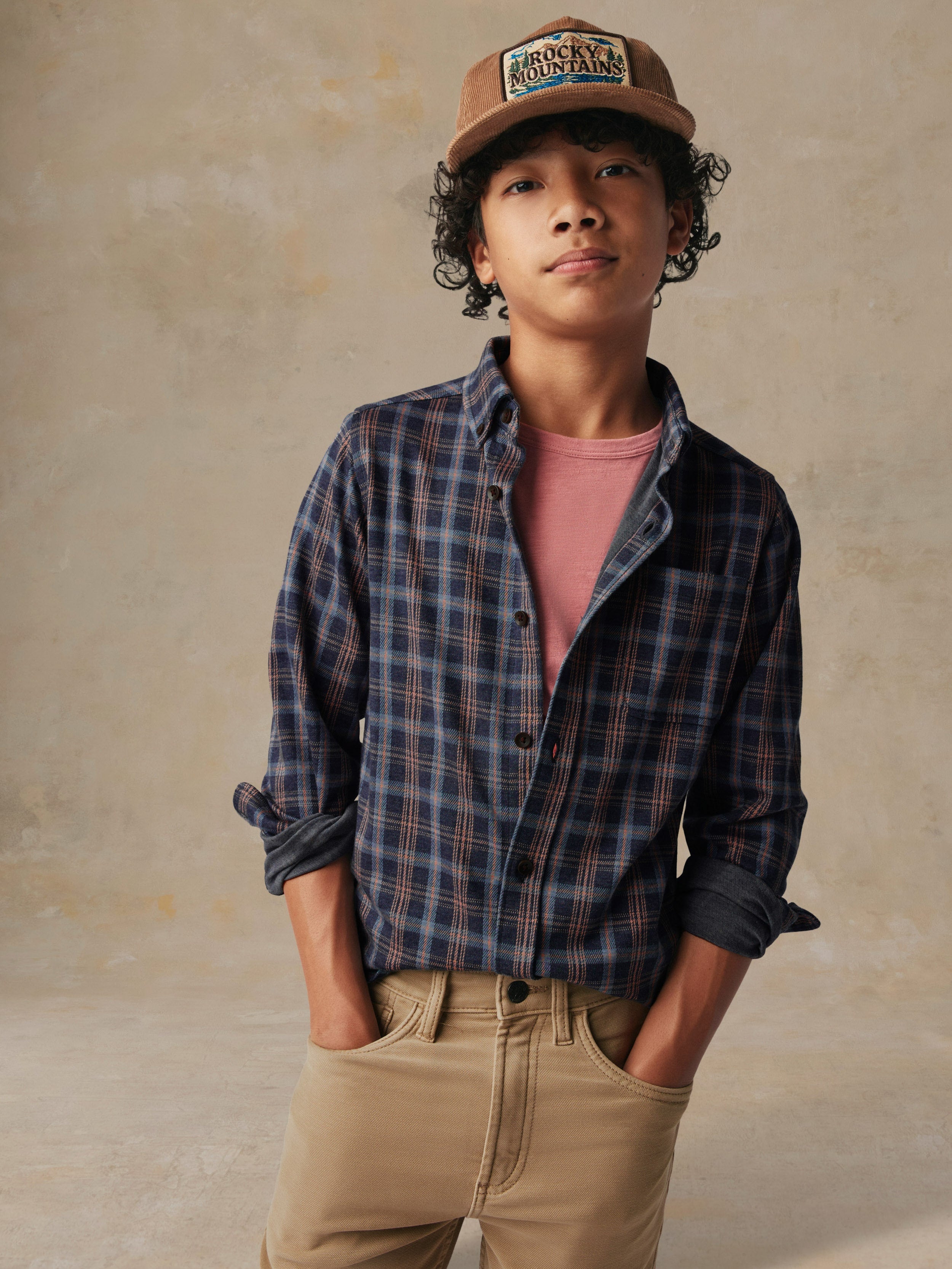 A child wearing a plaid button down shirt and beige pants