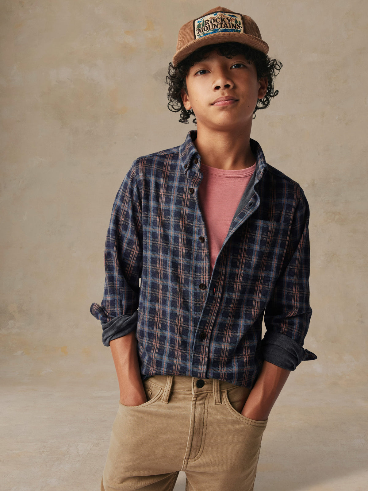 A child wearing a plaid button down shirt and beige pants, image 1 of 7