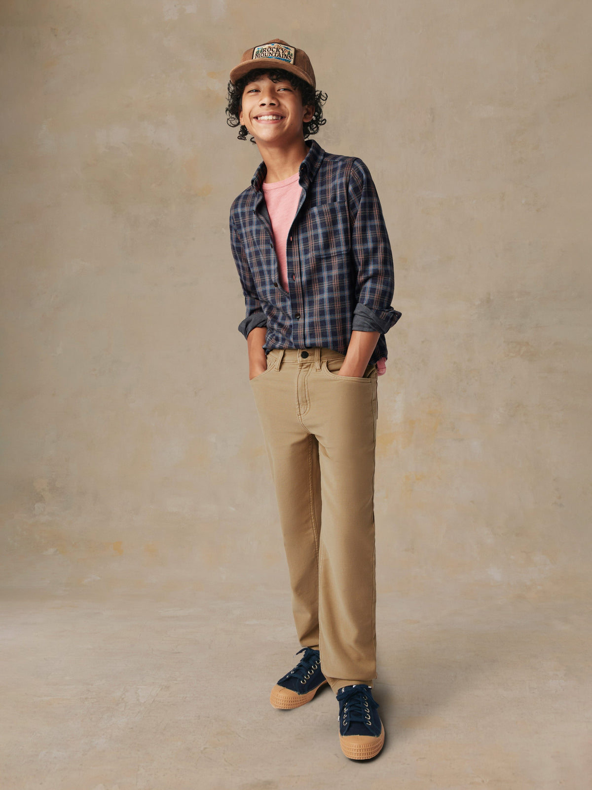 A child wearing a plaid button down shirt and beige pants, image 4 of 7