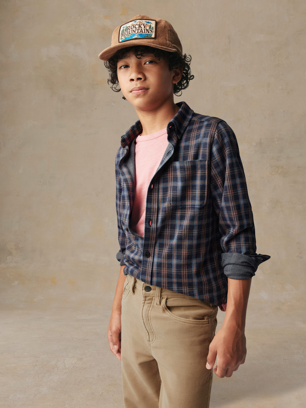 A child wearing a plaid button down shirt and beige pants, image 3 of 7