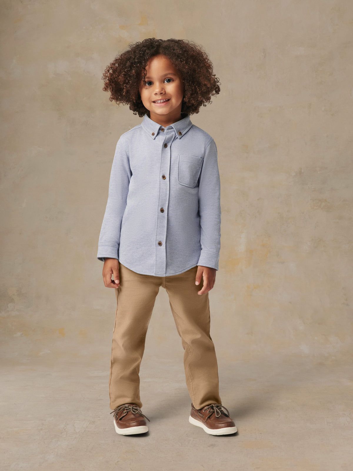 A child wearing a blue button up shirt and beige pants, image 1 of 6