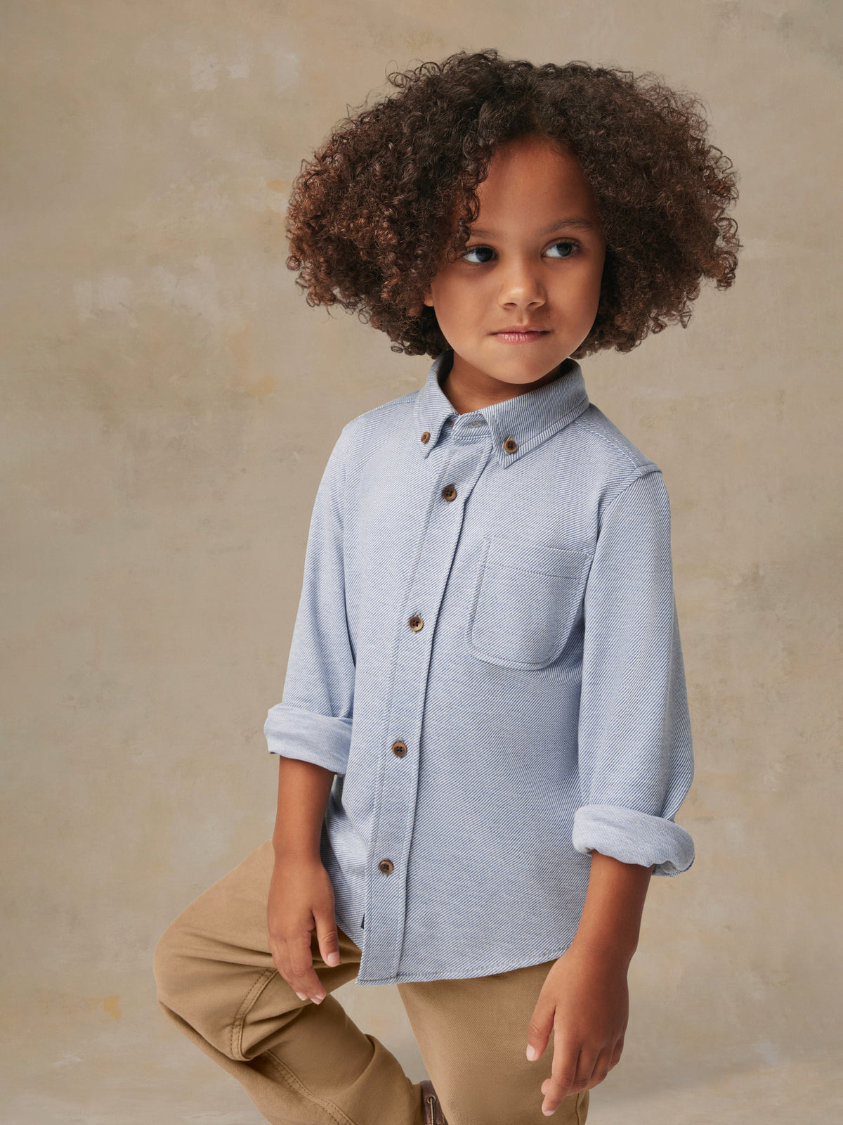 A child wearing a blue button up shirt and beige pants, image 2 of 6