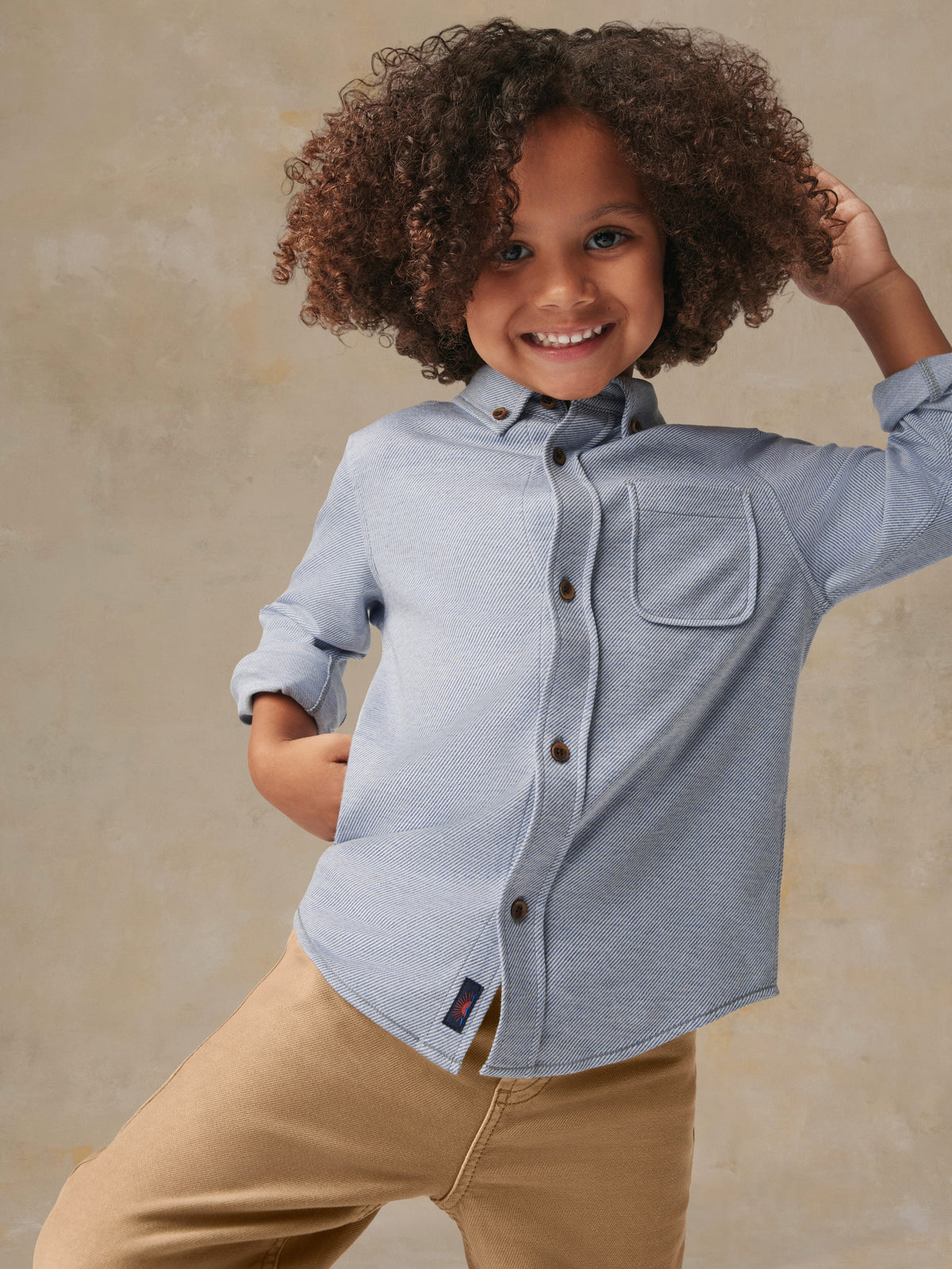 A child wearing a blue button up shirt and beige pants, image 4 of 6