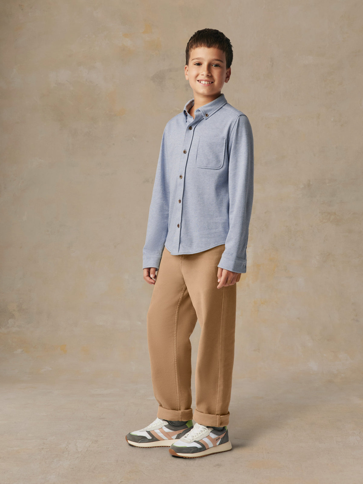 A child wearing a blue button up shirt and beige pants, image 6 of 7