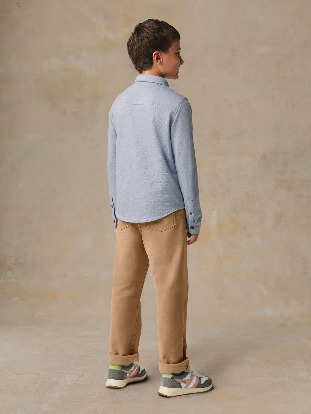 A child viewed from behind wearing a blue button up shirt and beige pants, image 5 of 7