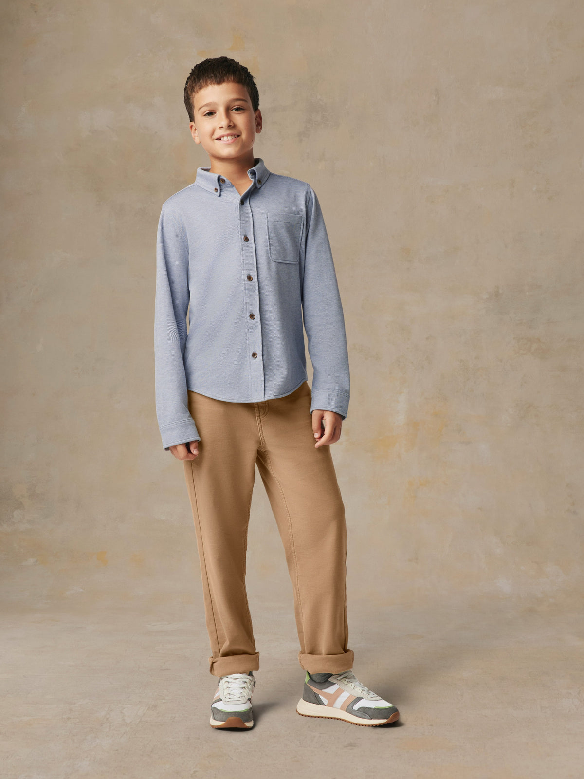 A child wearing a blue button up shirt and beige pants, image 2 of 7