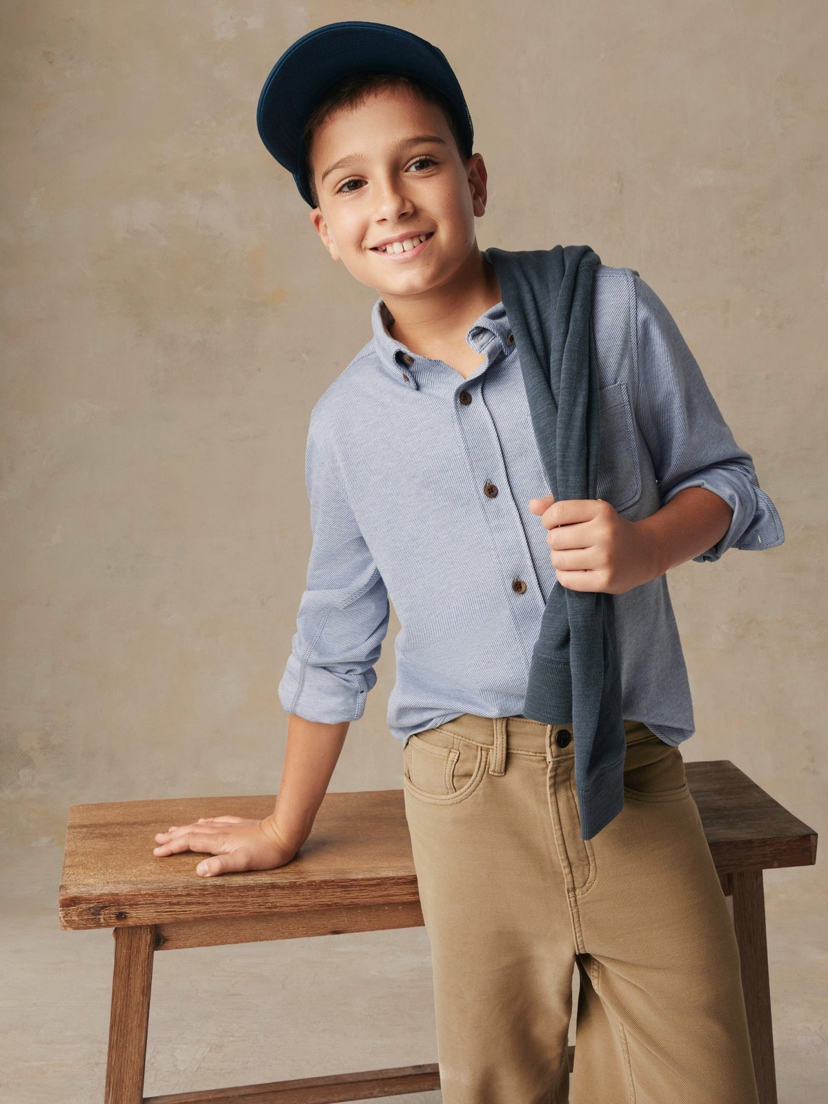 A child wearing a blue button up shirt and beige pants, image 3 of 7