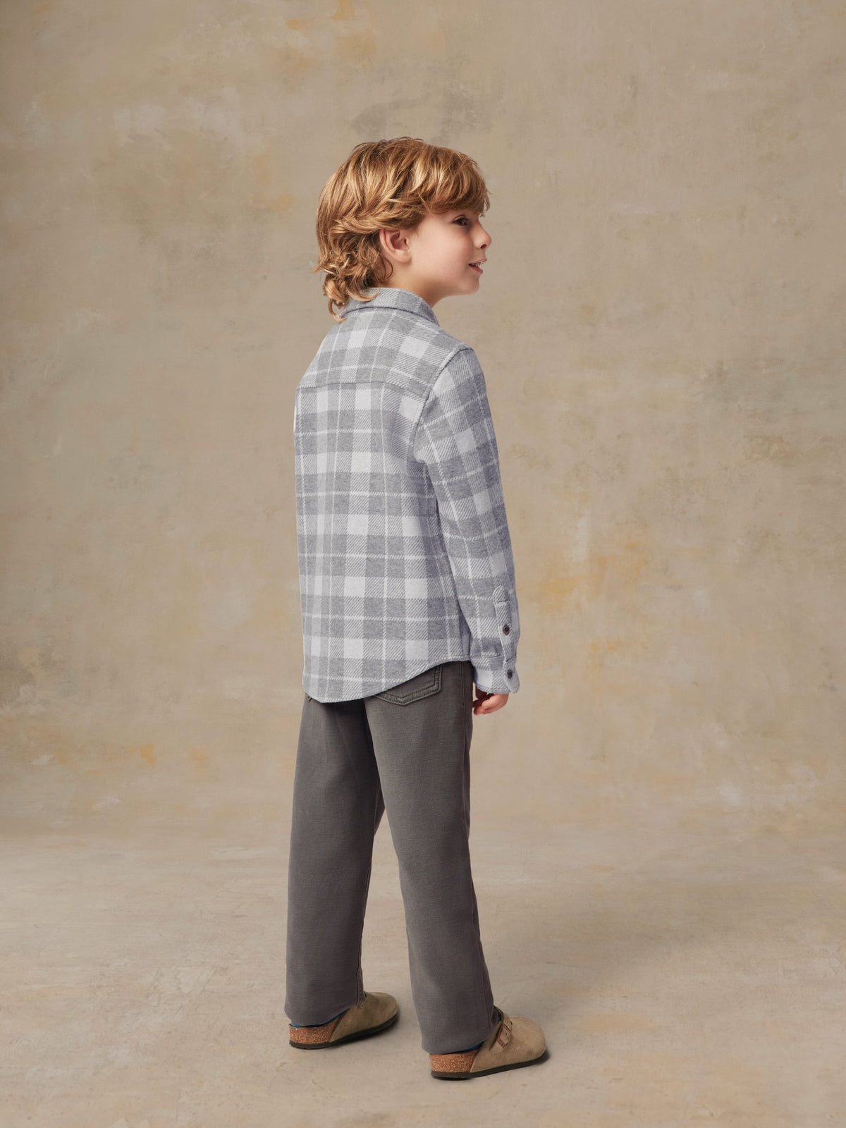 A child viewed from behind wearing a grey plaid button up shirt and grey pants, image 3 of 6