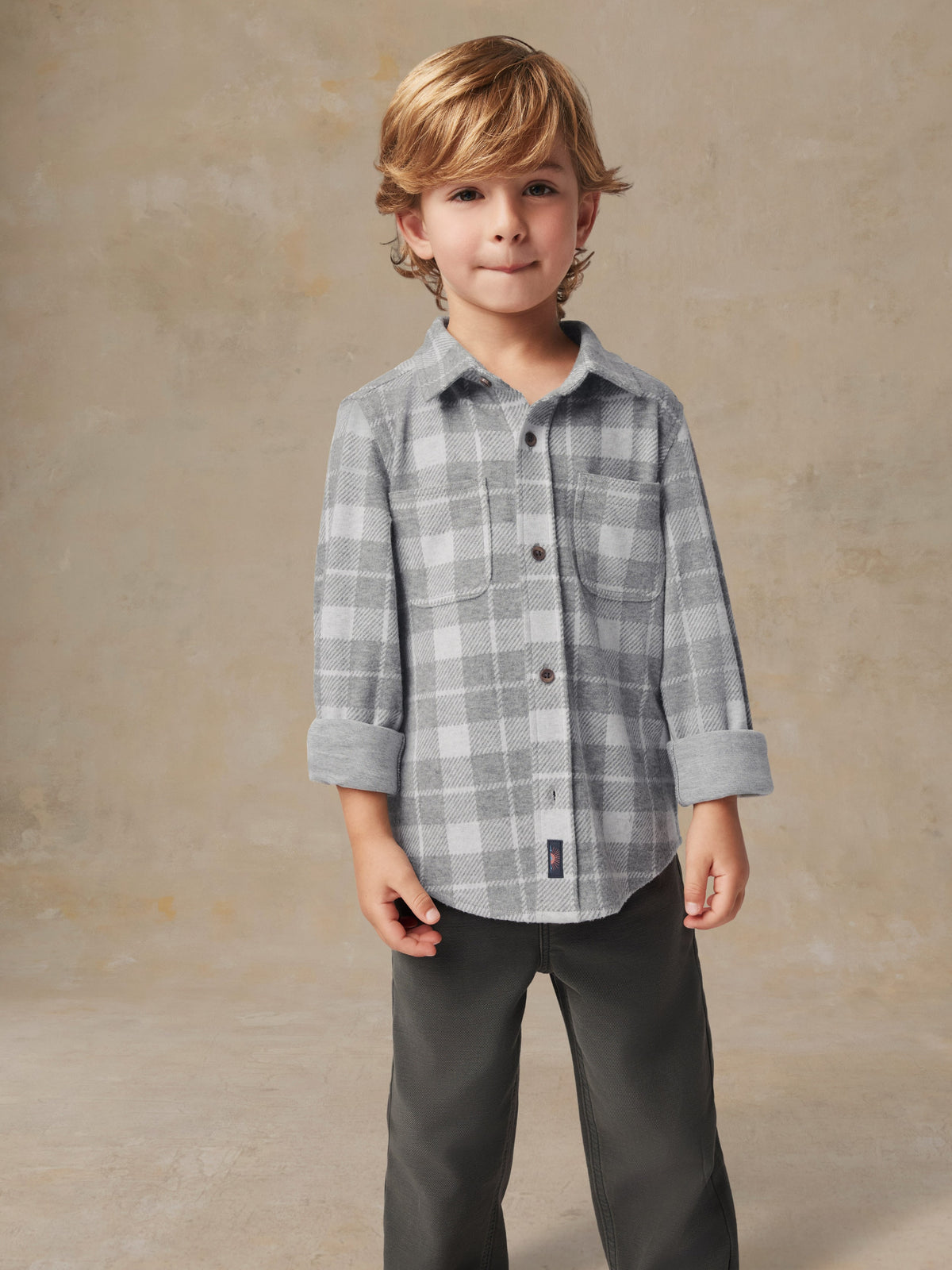 Close up of a child wearing a grey plaid button up shirt and grey pants, image 2 of 6