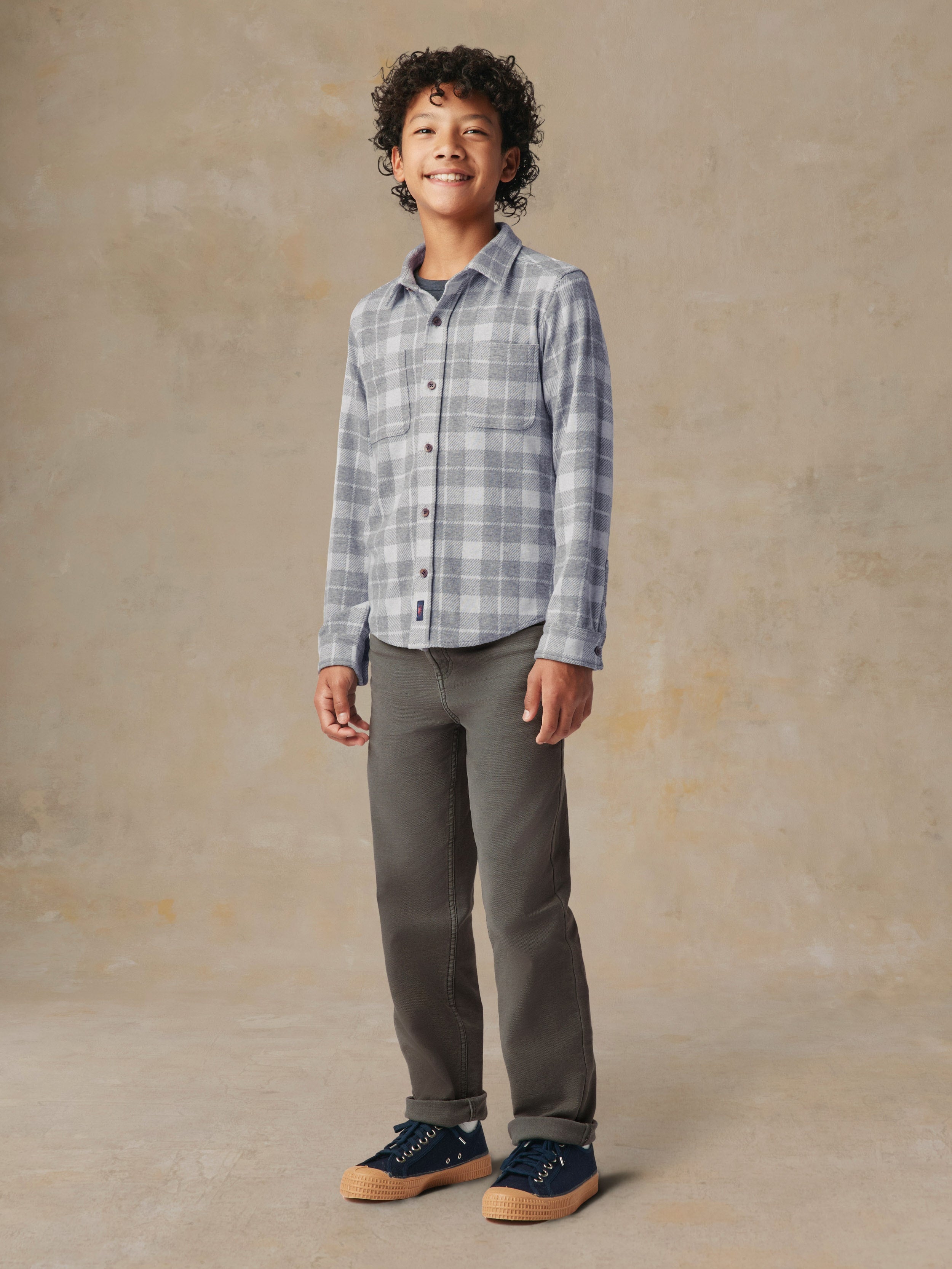 A child wearing a grey plaid button up shirt and grey pants