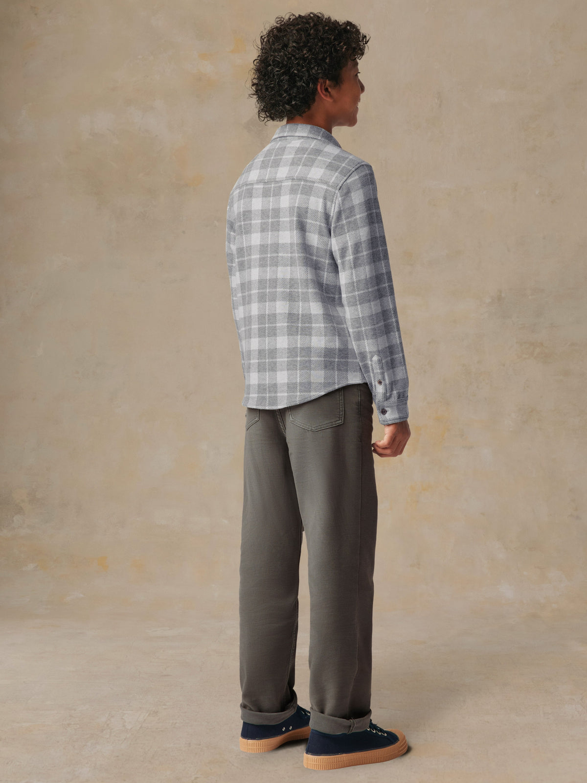 A child viewed from behind wearing a grey plaid button up shirt and grey pants, image 4 of 7