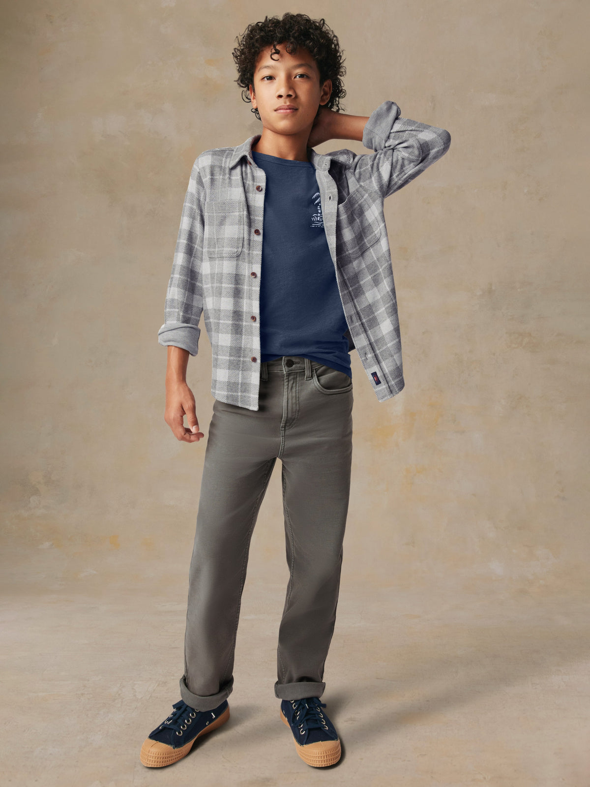 A child wearing a grey plaid button up shirt and grey pants, image 5 of 7