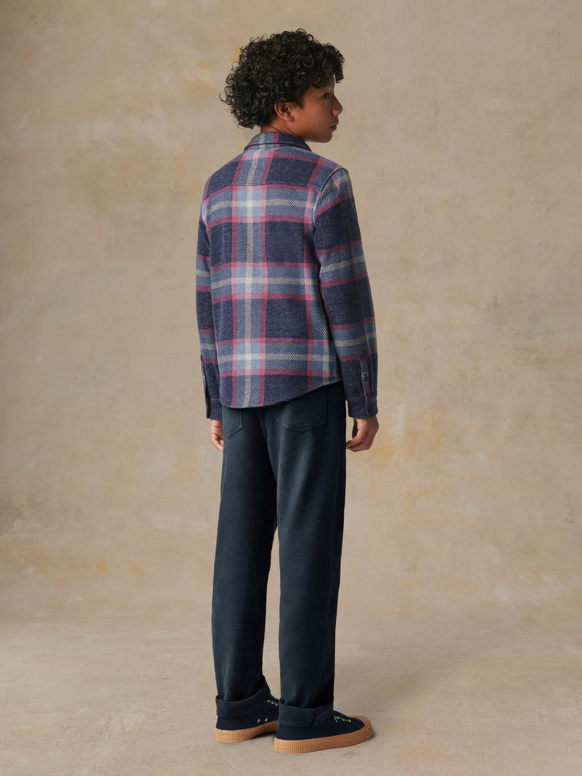 A child viewed from behind wearing a plaid button up shirt and black pants, image 5 of 6