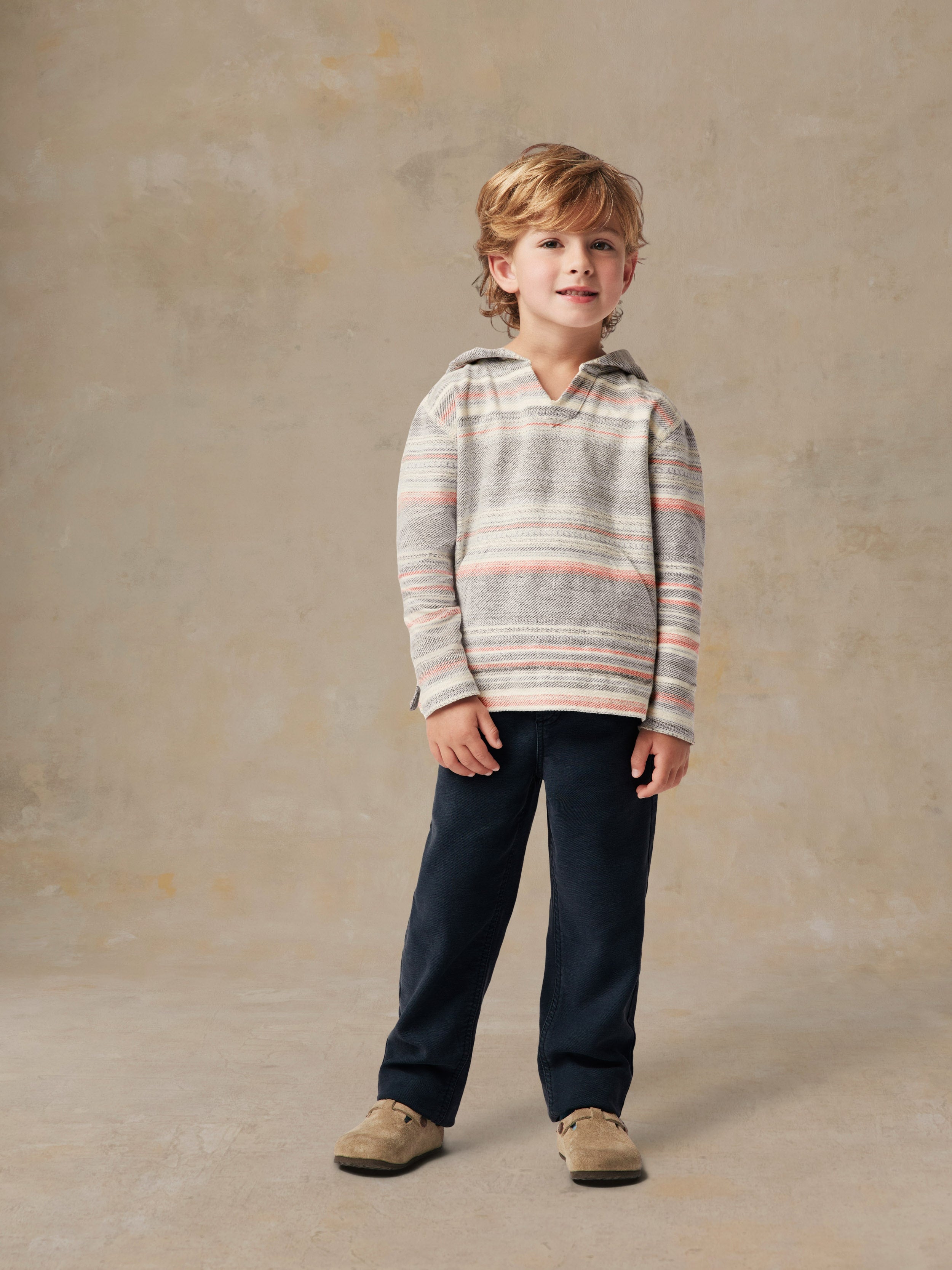 A boy wearing a striped hoodie and blue pants