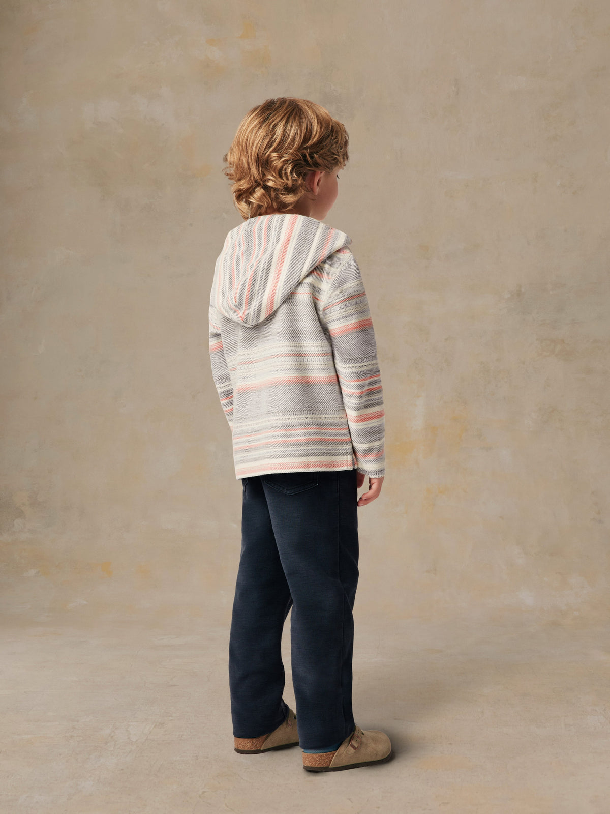 A boy viewed from behind wearing a striped hoodie and blue pants, image 4 of 4