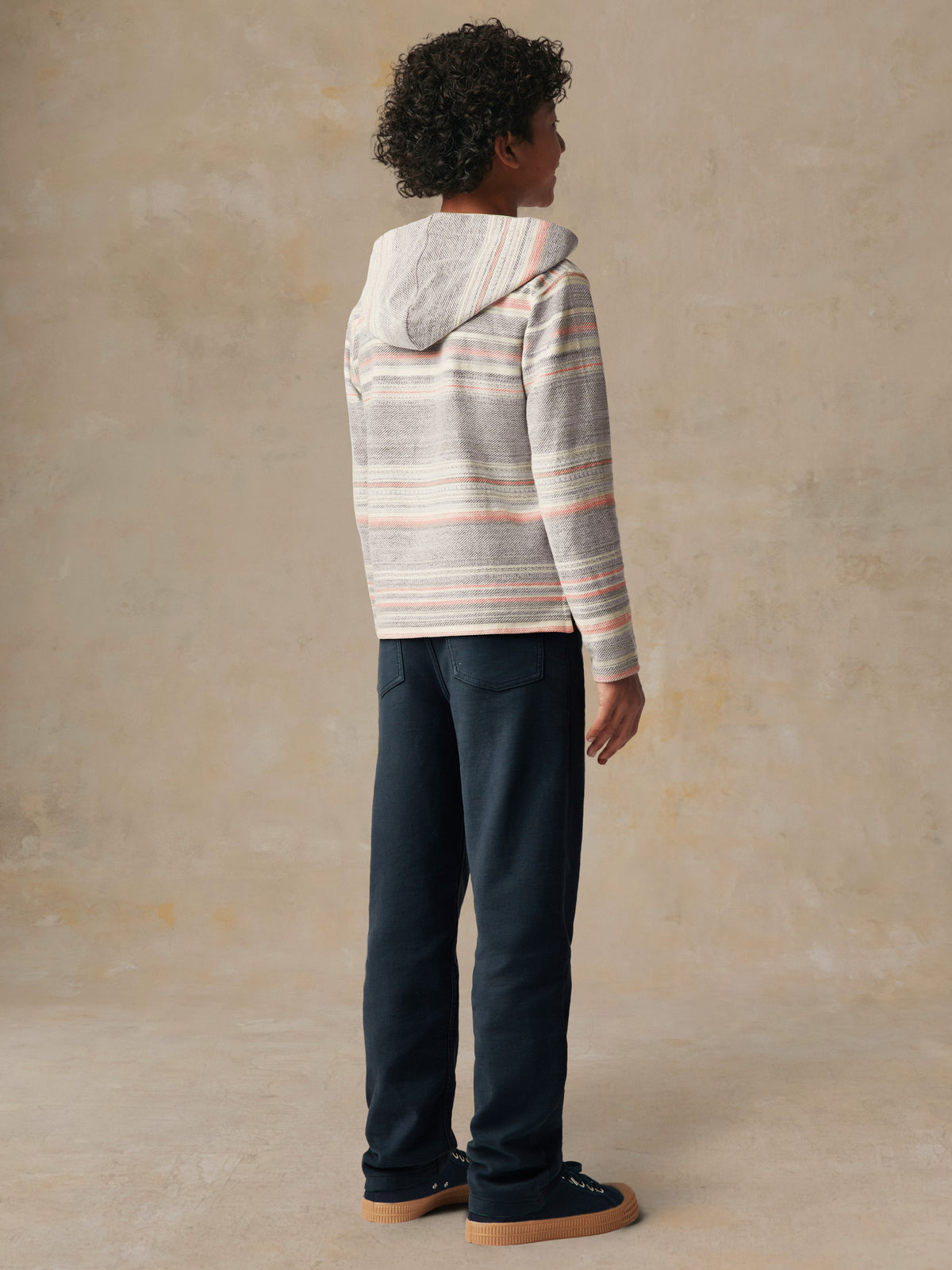 A kid viewed from behind wearing a striped hoodie and blue pants, image 3 of 5