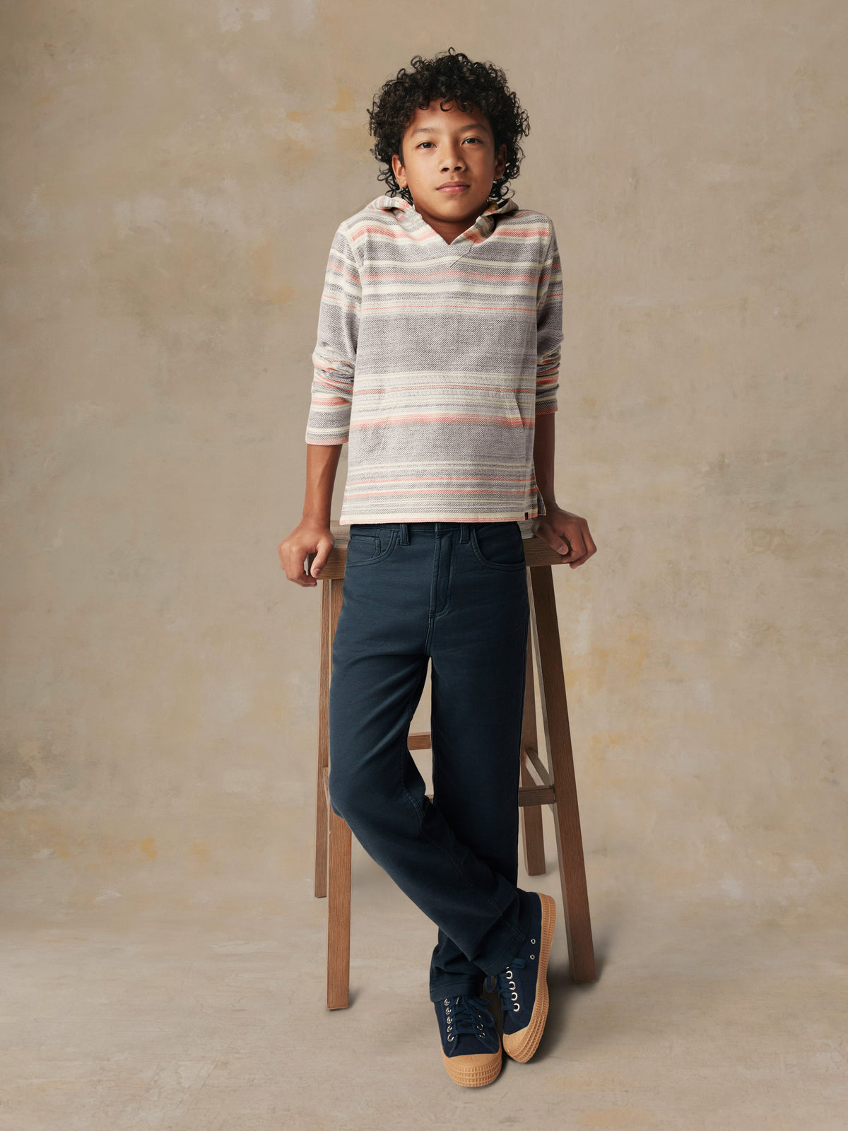 A kid wearing a striped hoodie and blue pants, image 2 of 5