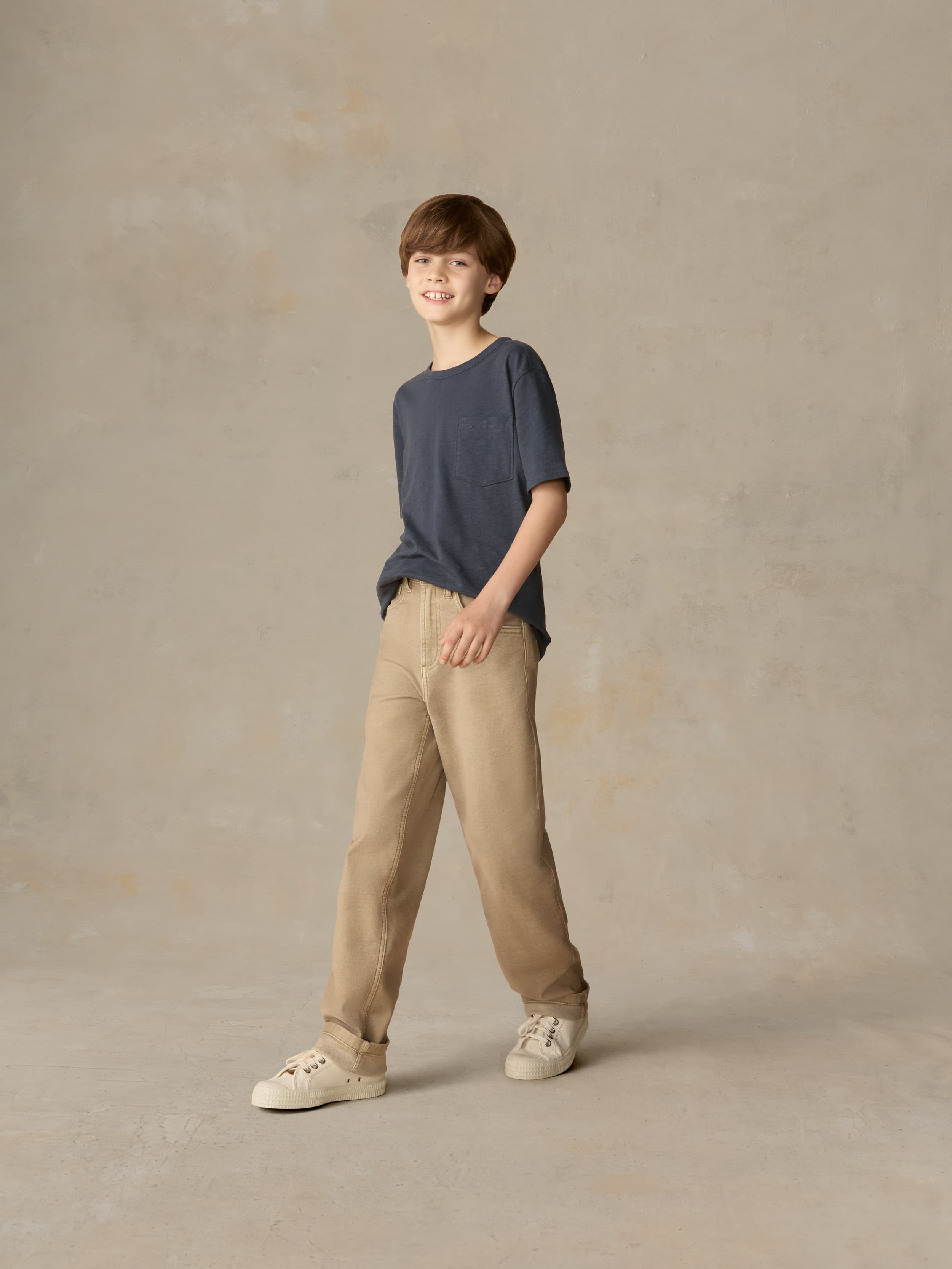 Child wearing a blue t-shirt and beige pants against a beige background