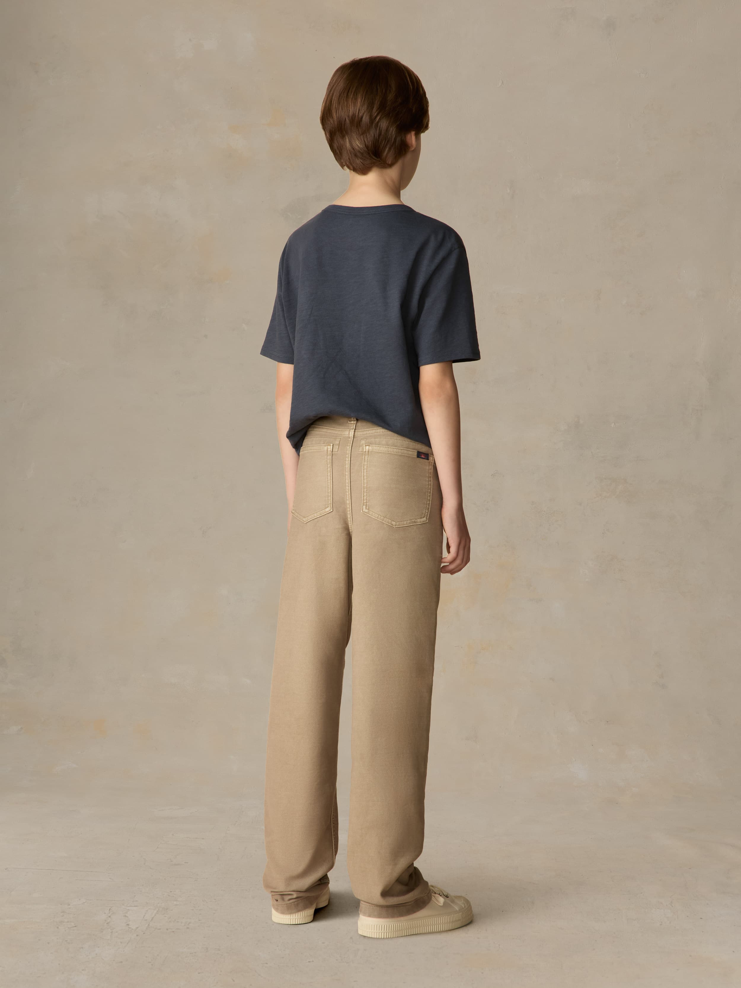 Child wearing a blue t-shirt and beige pants against a beige background