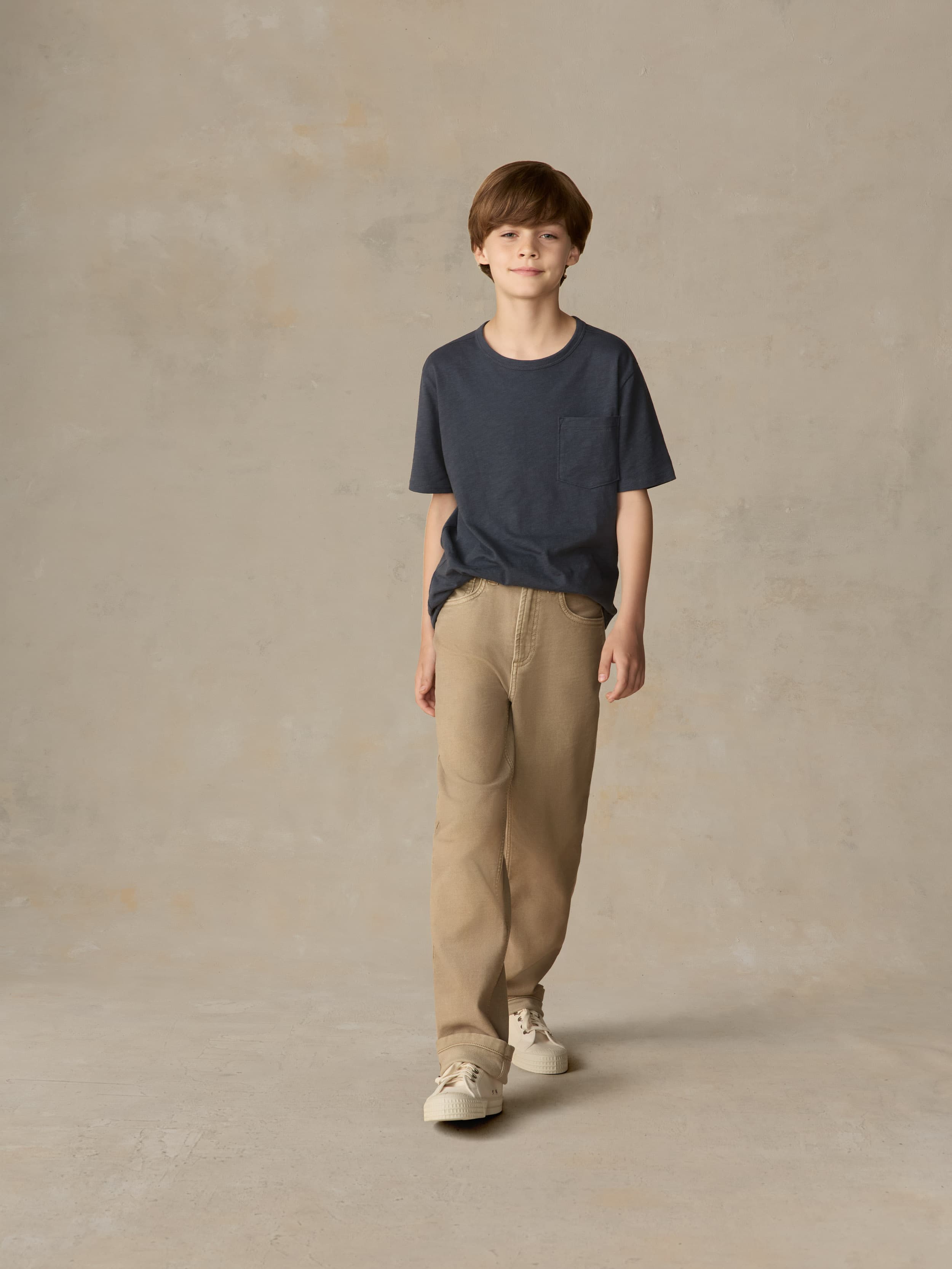 Child wearing a blue t-shirt and beige pants against a beige background