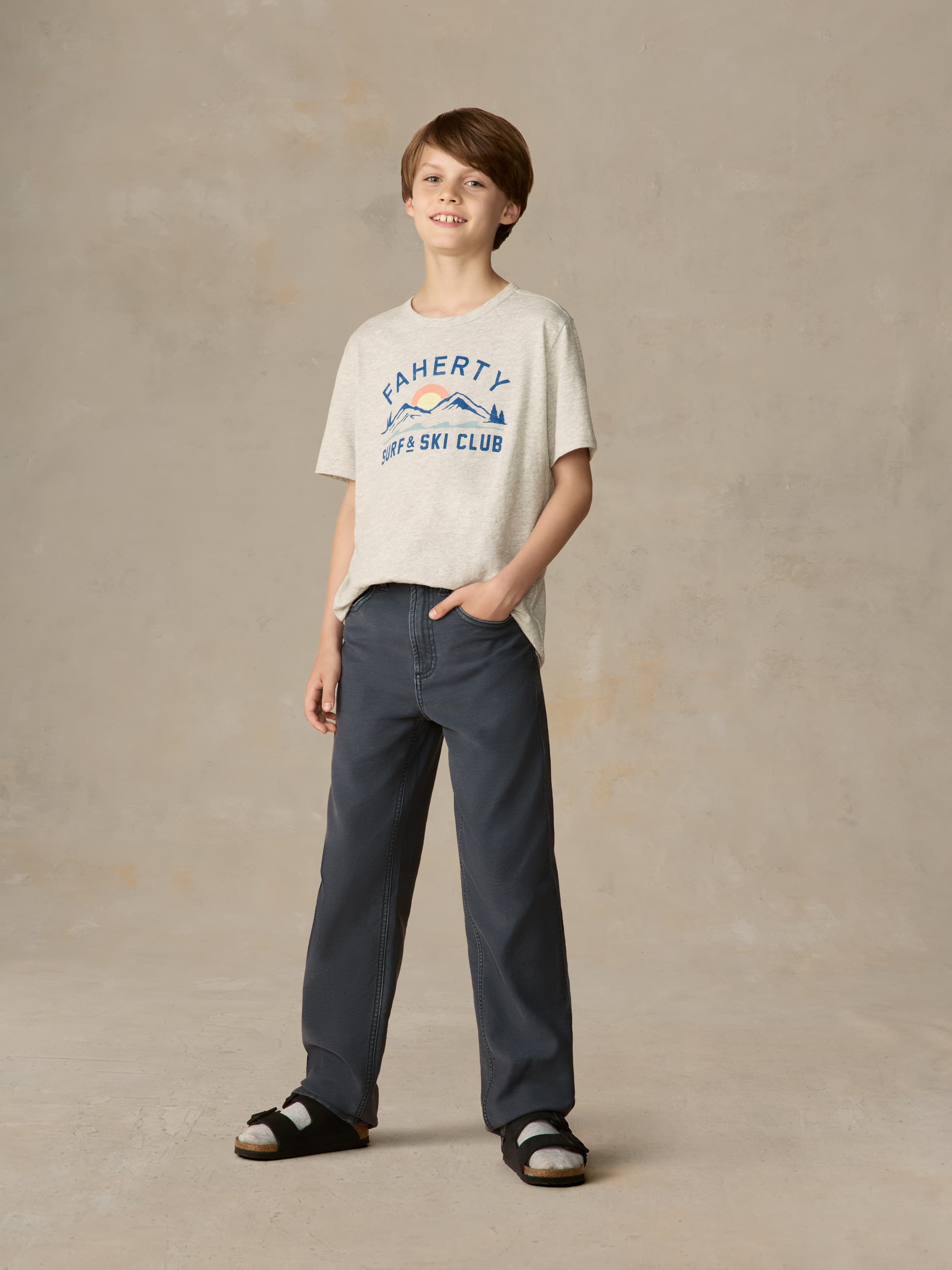 Child wearing a grey graphic tee with navy pants against a beige background