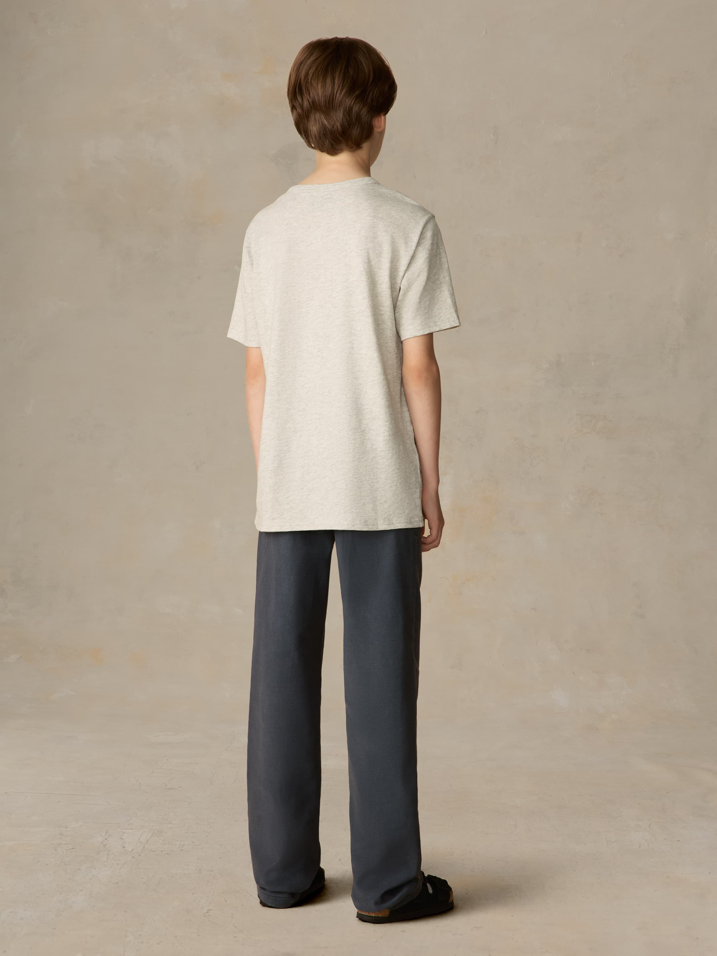 Child wearing a grey tee with navy pants against a beige background