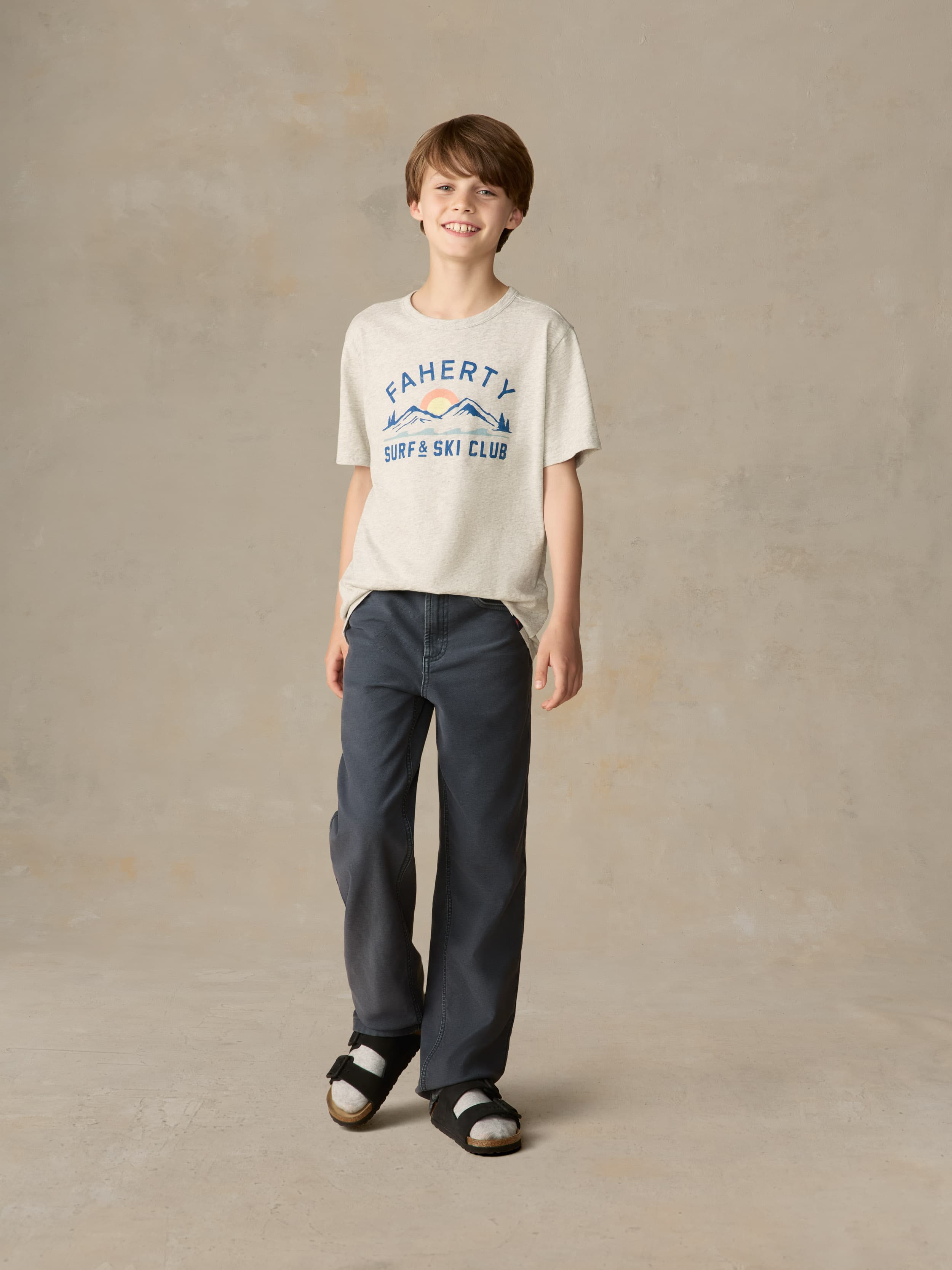 Child wearing a grey graphic tee with navy pants against a beige background