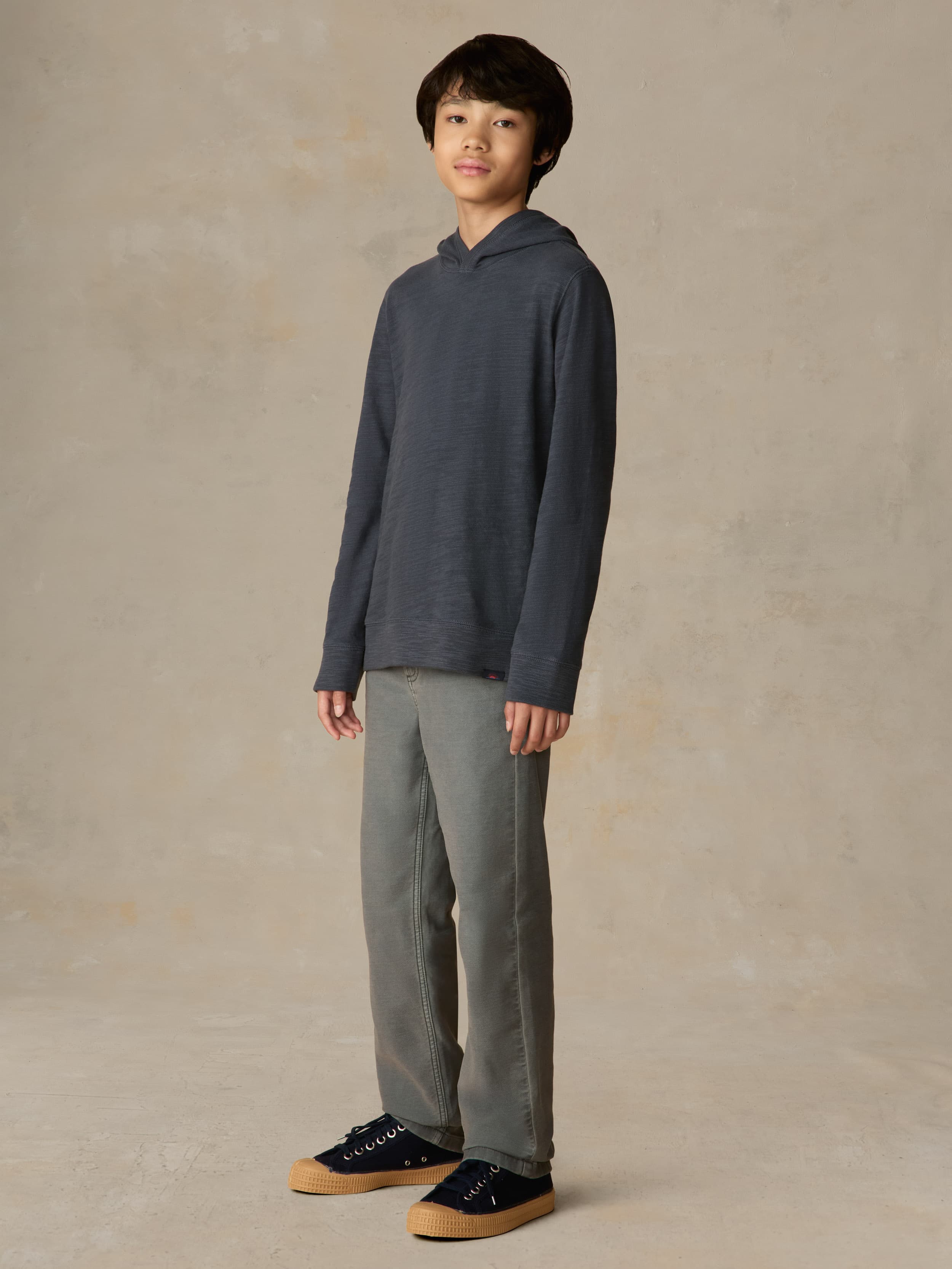 Child wearing a blue hoodie with grey pants against a beige background
