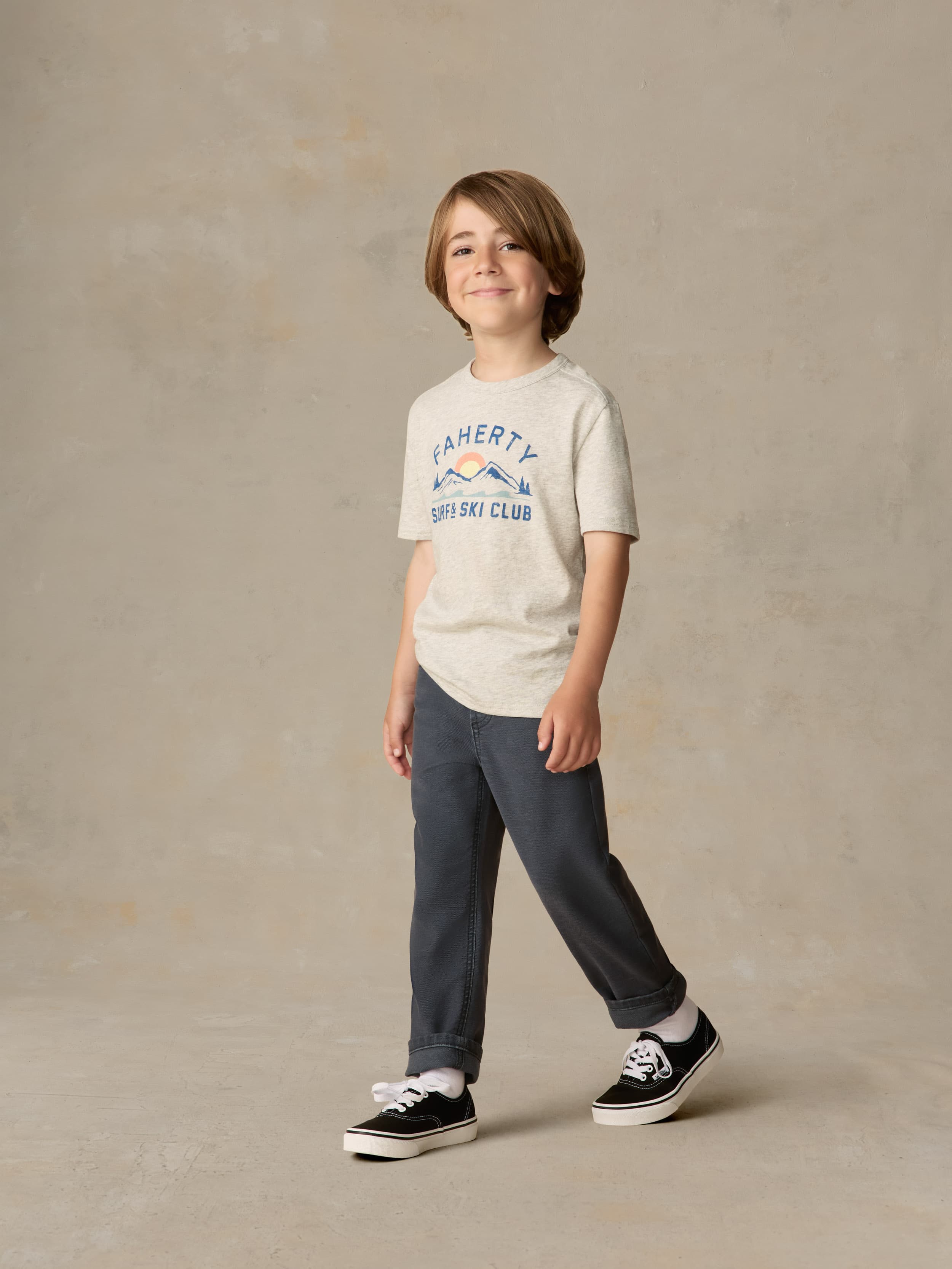Child wearing graphic grey tee and navy pants against a beige background