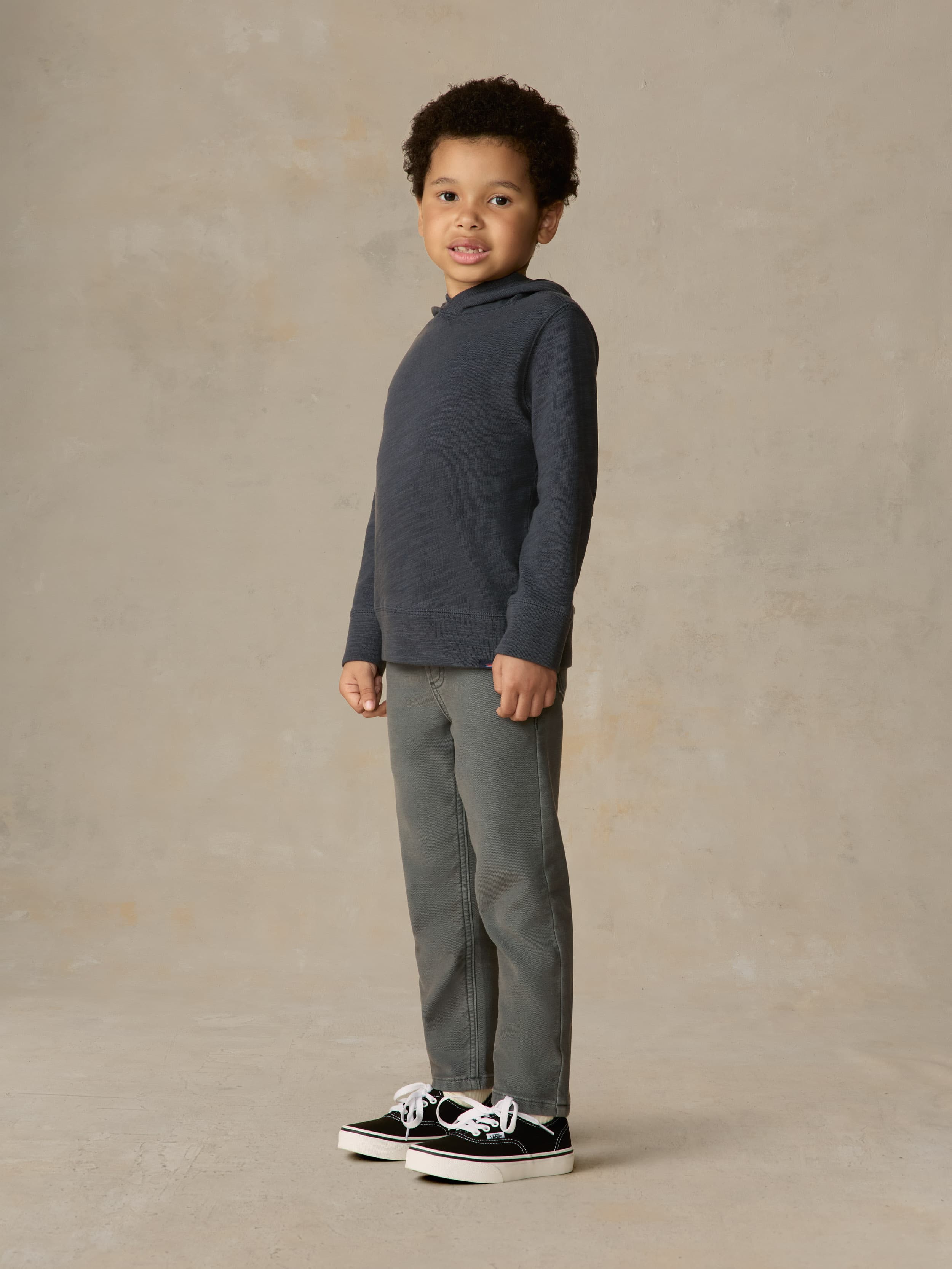 Child wearing blue hoodie and grey pants against a beige background