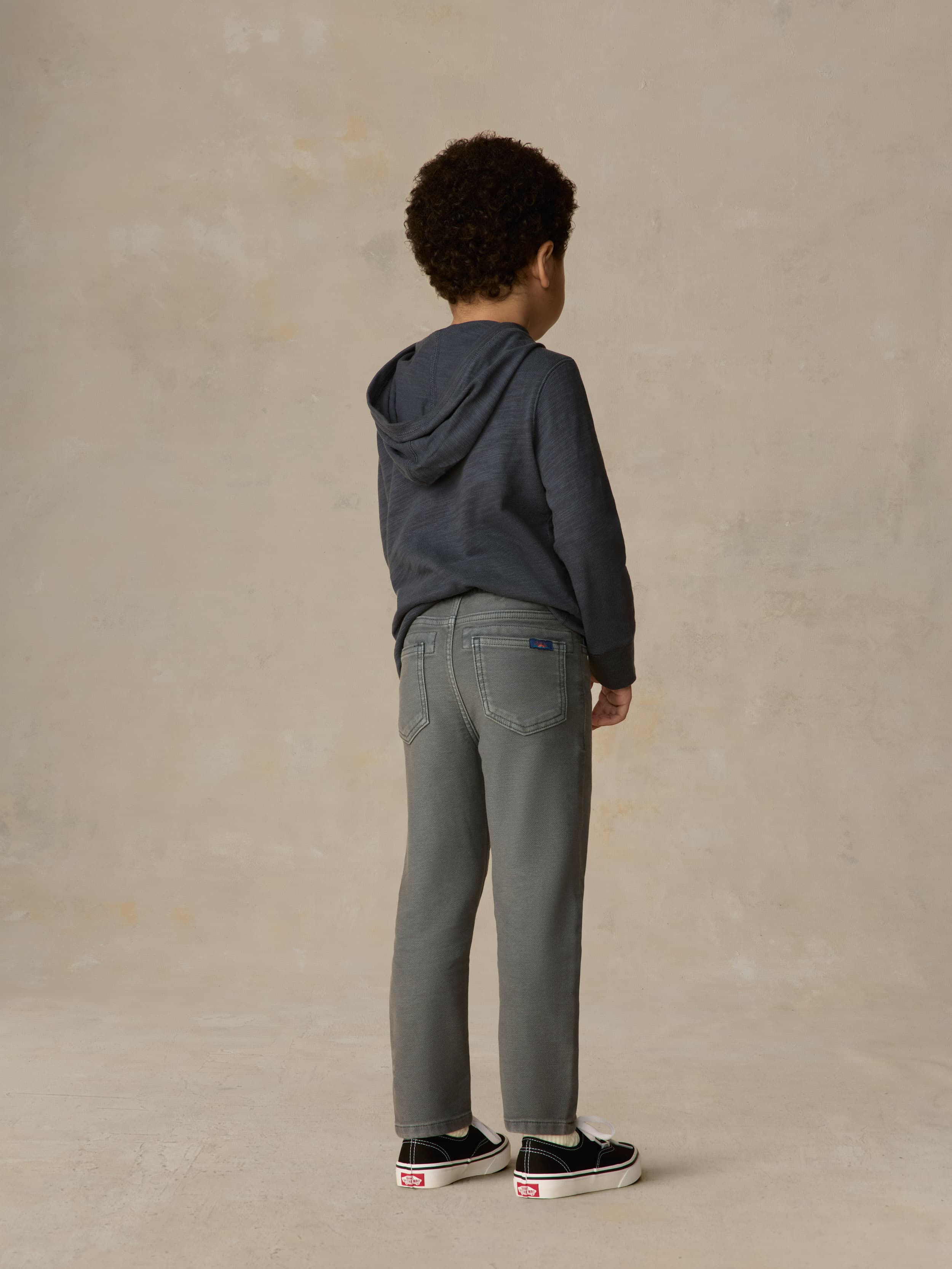 Child wearing blue hoodie and grey pants against a beige background