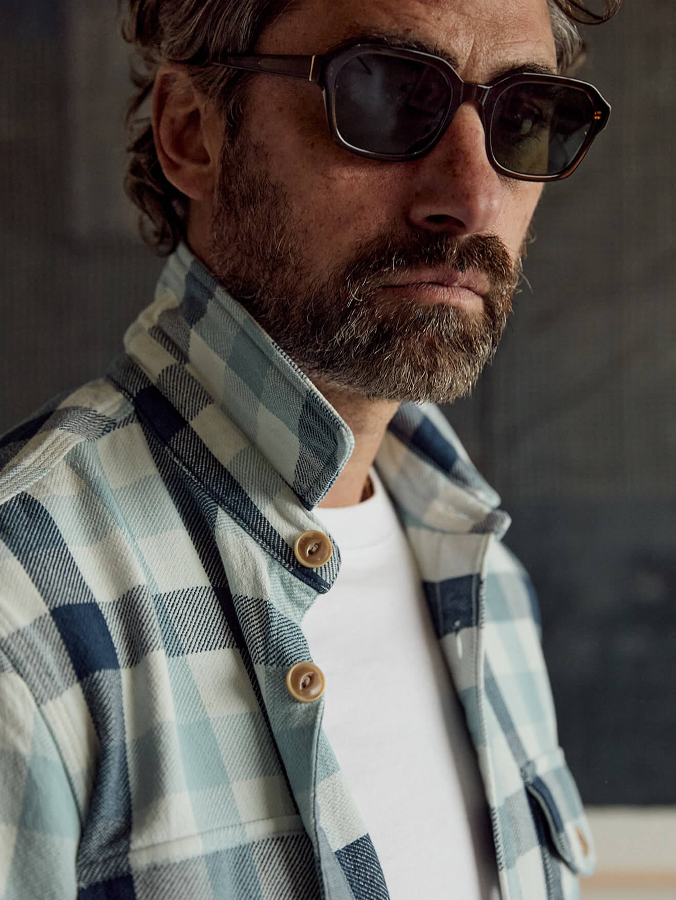 A male model wearing a plaid work shirt over a white tee with sunglasses