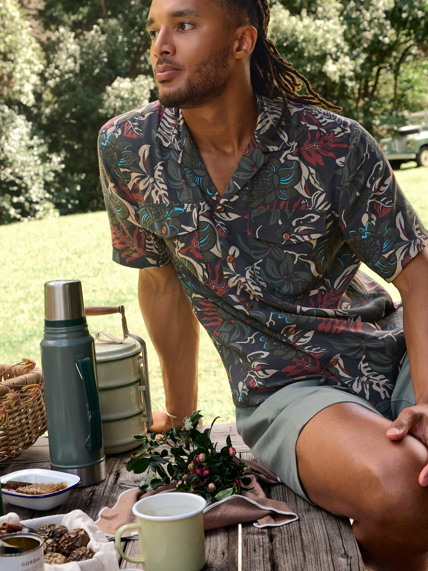 Man sitting at a picnic table with a floral shirt, surrounded by nature.