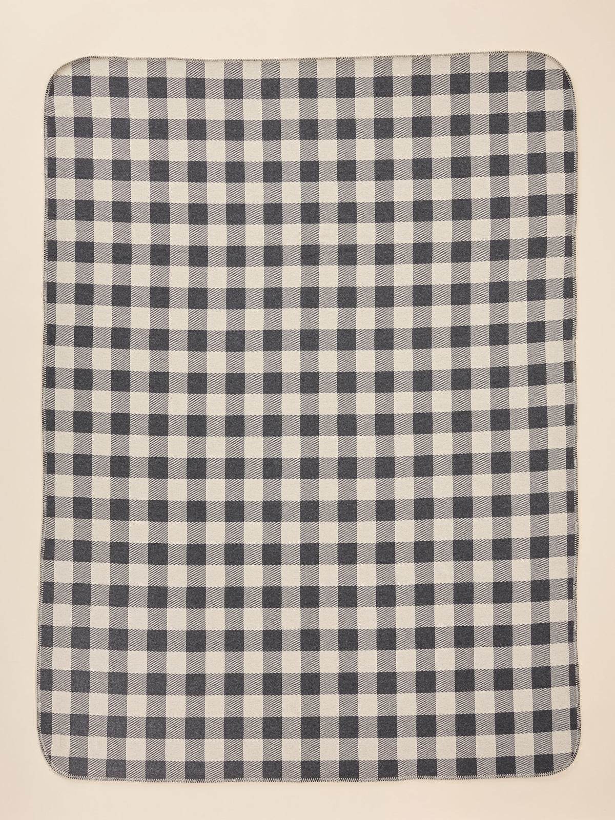 A rectangular blanket with a classic navy and off-white gingham checkered pattern, shown flat against a light beige background., image 3 of 3