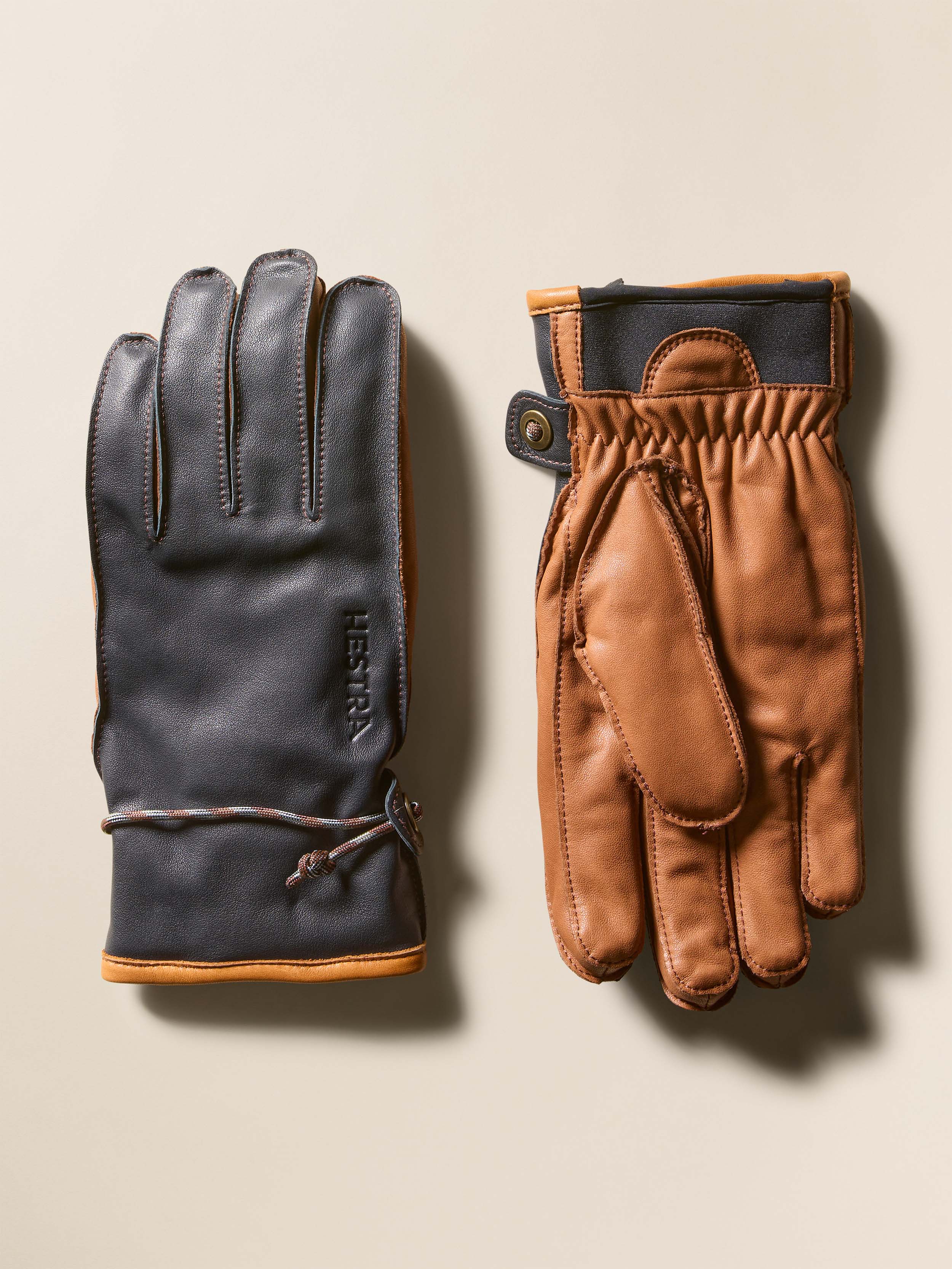 Pair of dark navy and brown leather gloves on a beige background