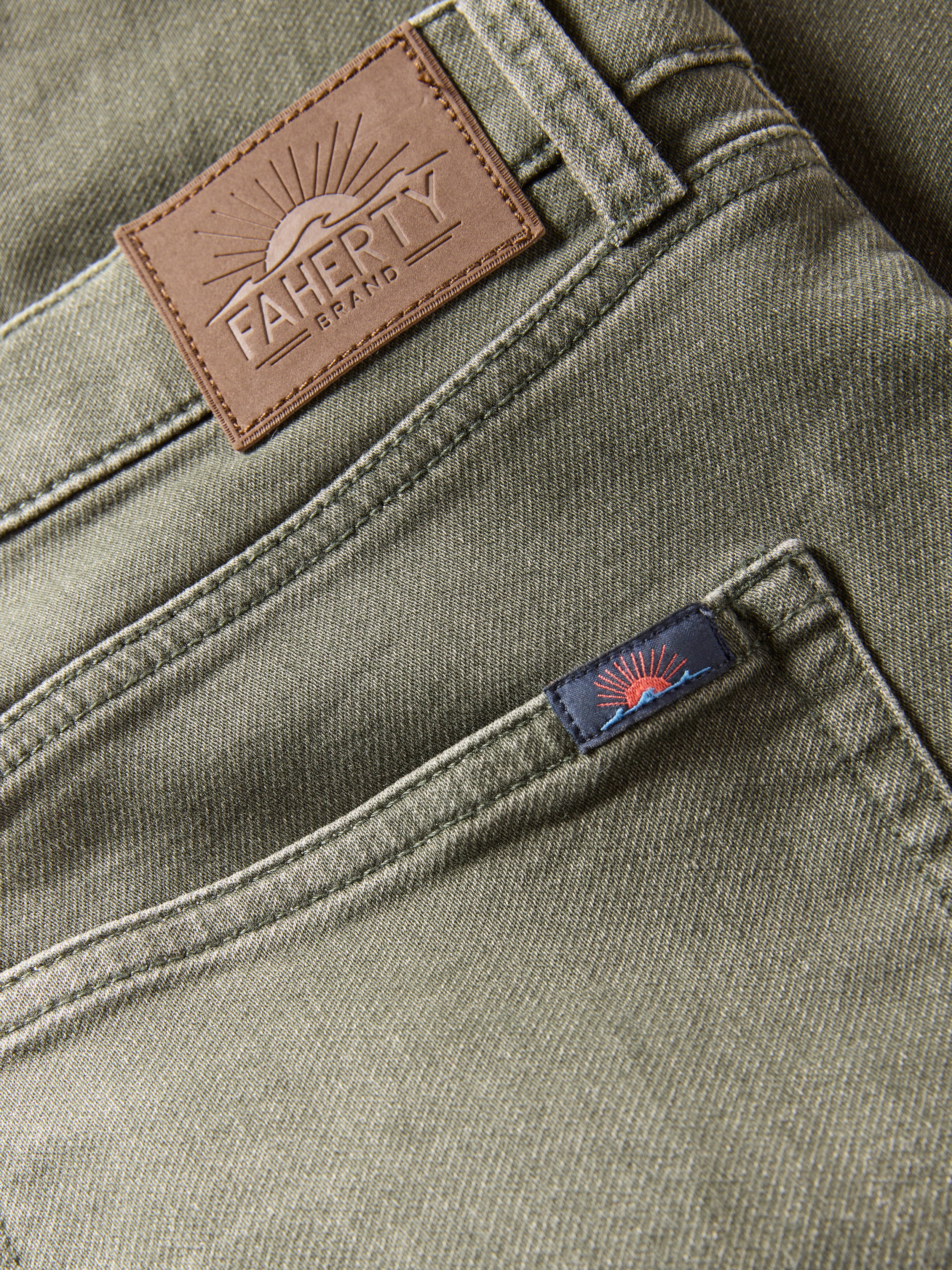Close-up of green pants with a brown leather patch and blue label on a dark background