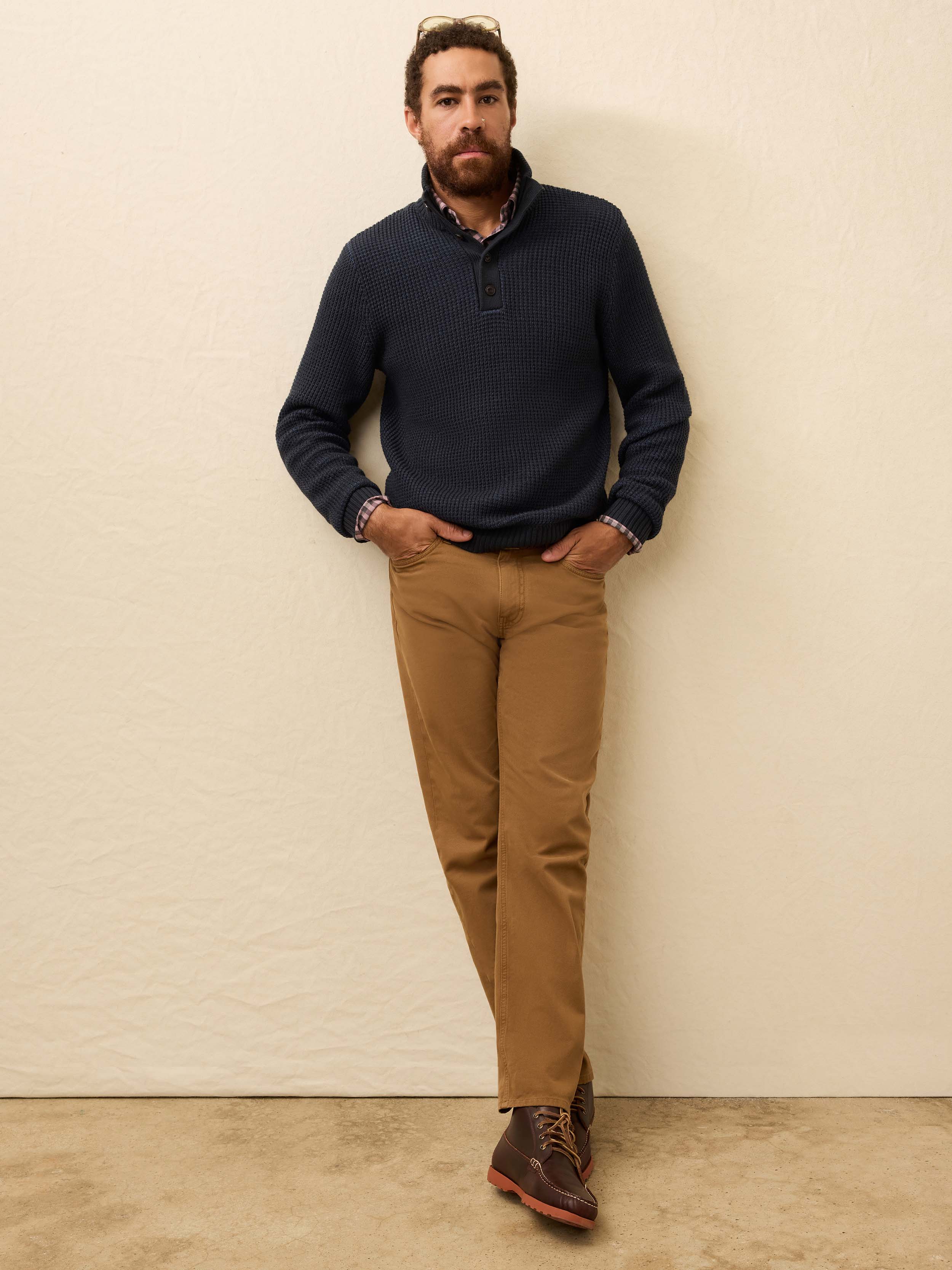 Man is wearing tan twill pants with a navy cardigan against a beige background