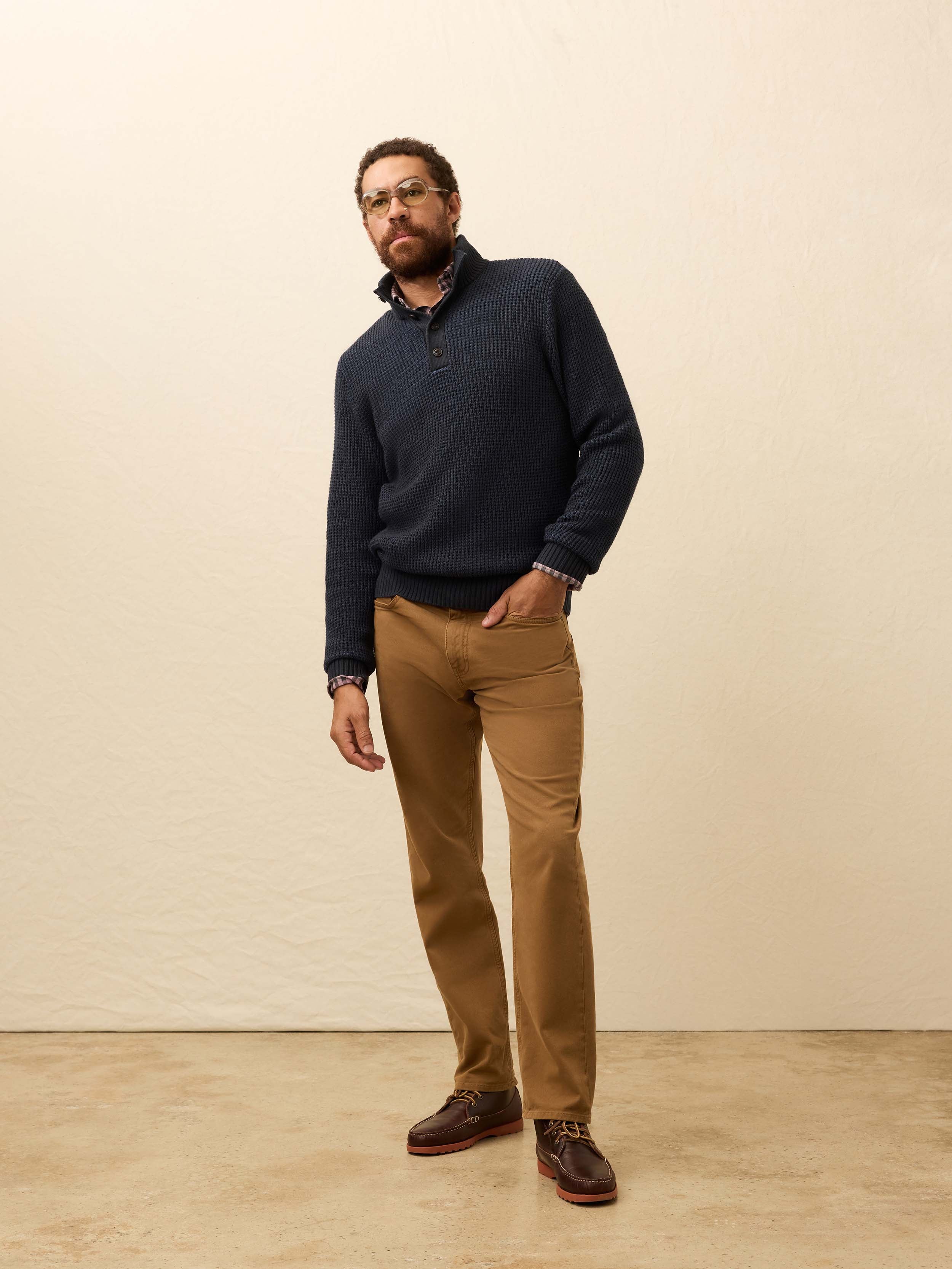 Man is wearing tan twill pants with a navy cardigan against a beige background