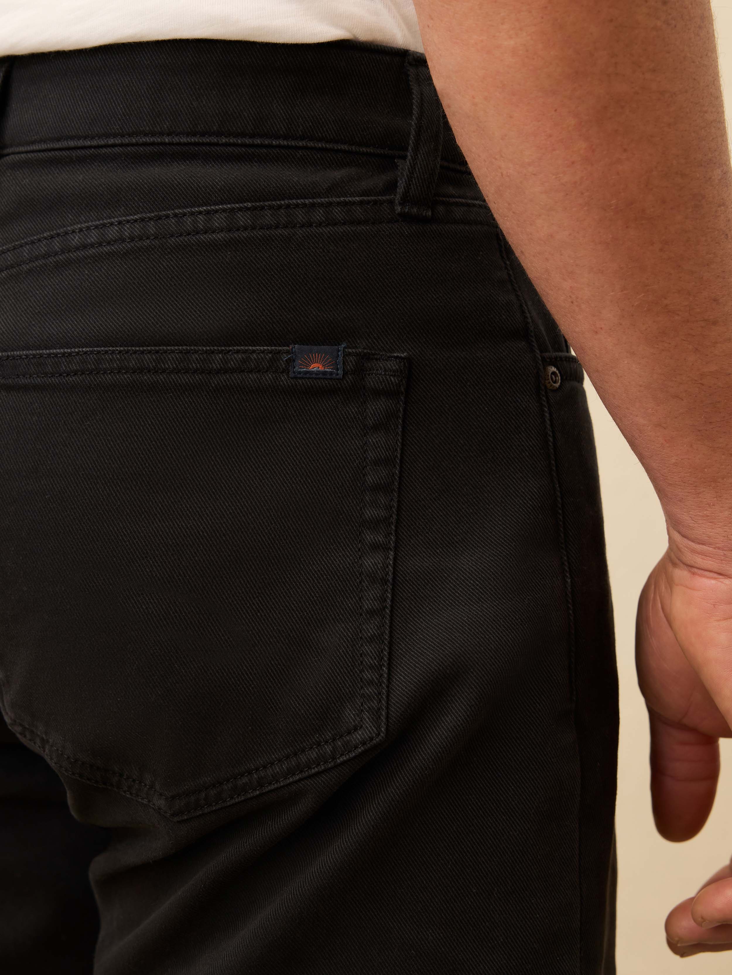 Close-up of black pants with a visible  Faherty brand logo on a beige background